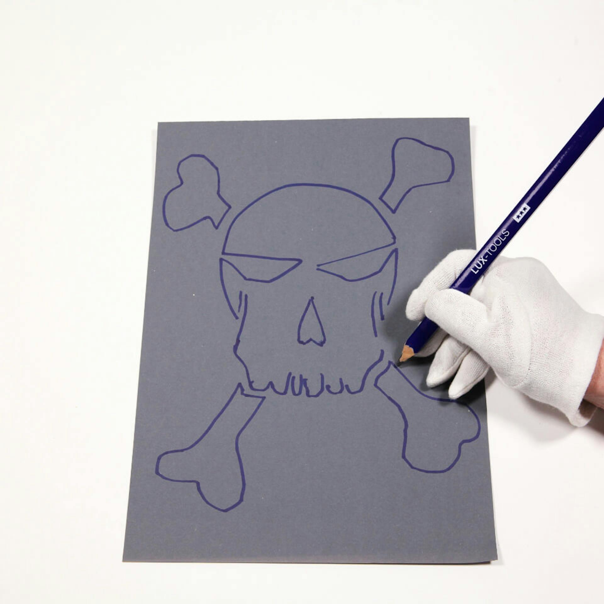 Eine Person zeichnet die Umrisse eines Totenkopfes auf eine Pappe.