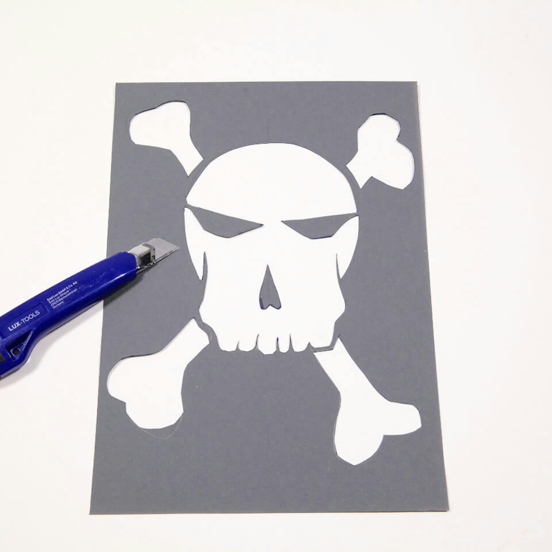 Eine Person schneidet die Form eines Totenkopfes aus einer Pappe aus.