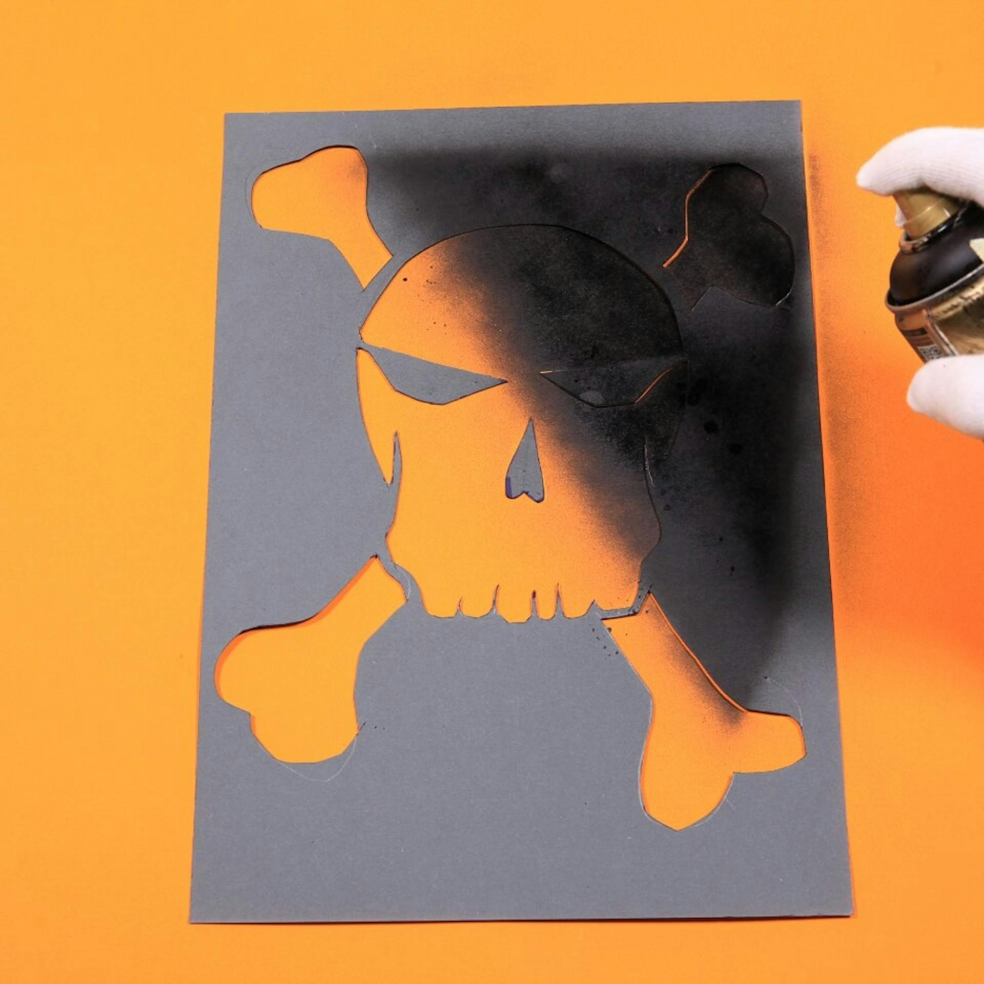 Eine Person sprüht schwarze Sprühfarbe über die Schablone.