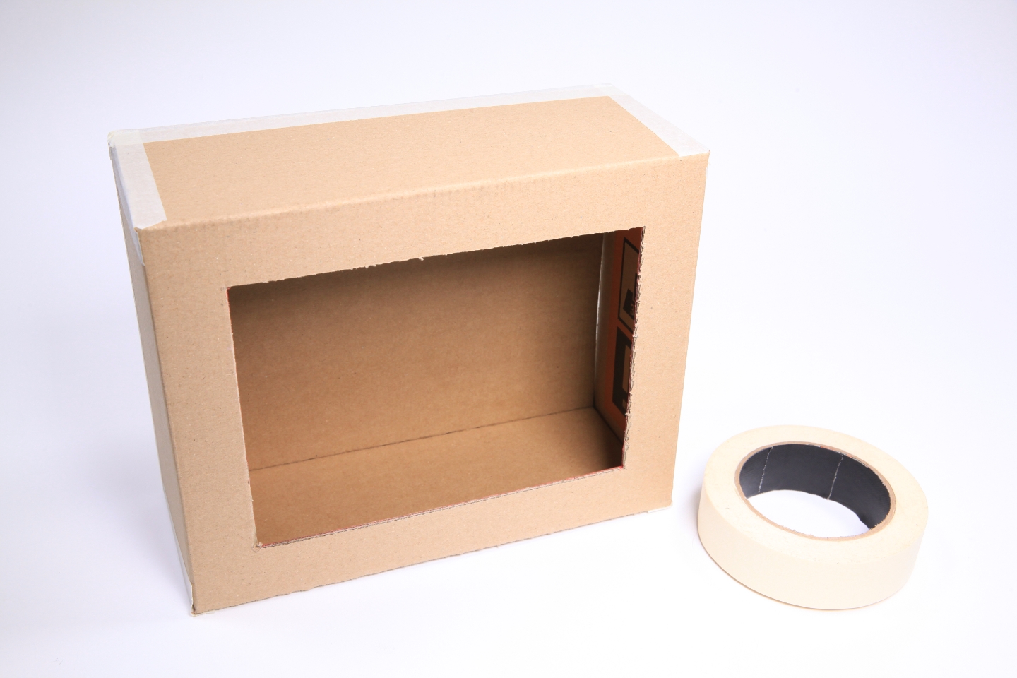 Als Box mit Öffnung zusammengefalteter Karton liegt neben Kreppband.
