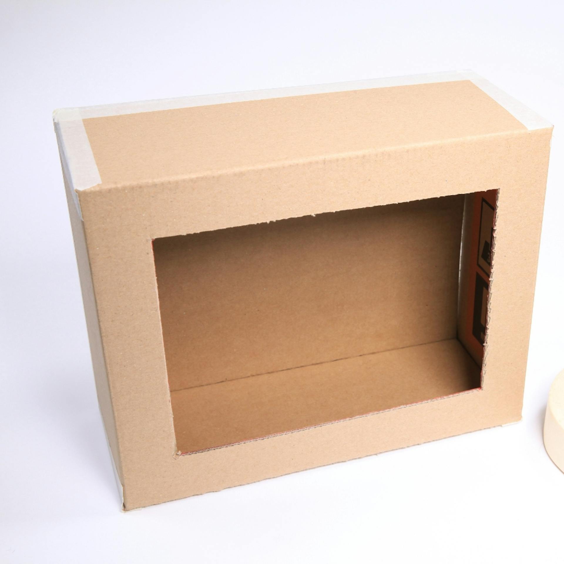 Als Box mit Öffnung zusammengefalteter Karton liegt neben Kreppband.