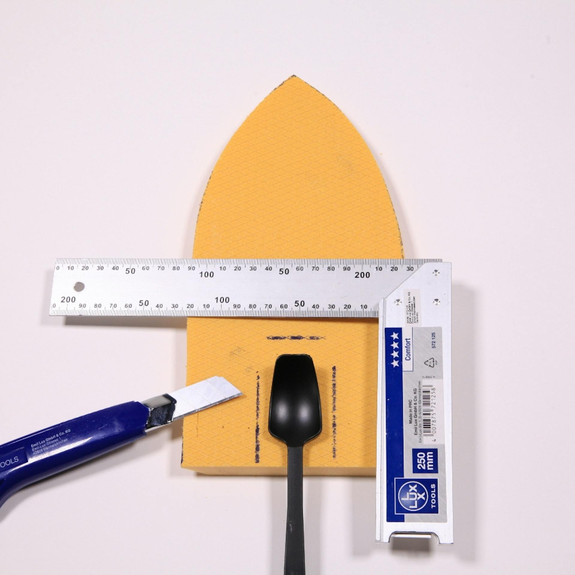 Cutter liegt neben Plastiklöffel und Winkel auf Schiff-Form aus Dämmplatte