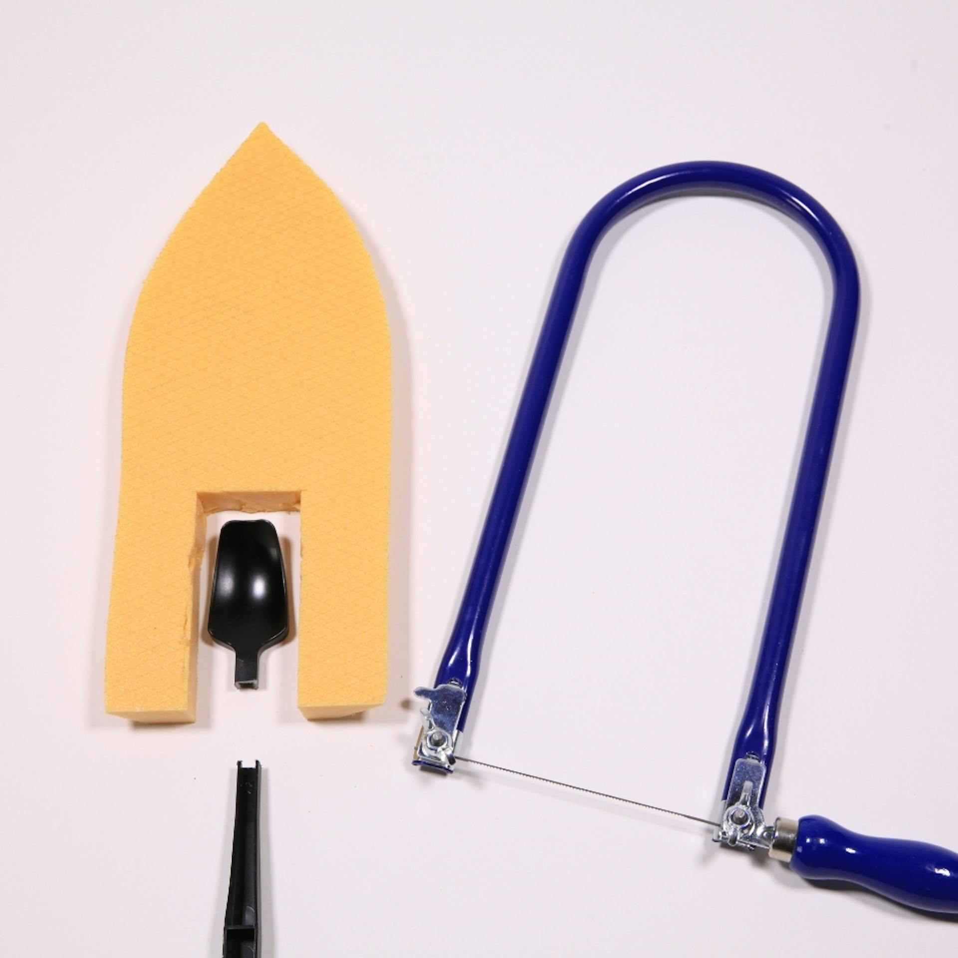 Schiff-Form aus Dämmplatte und durchgesägter Löffel liegen neben Laubsäge