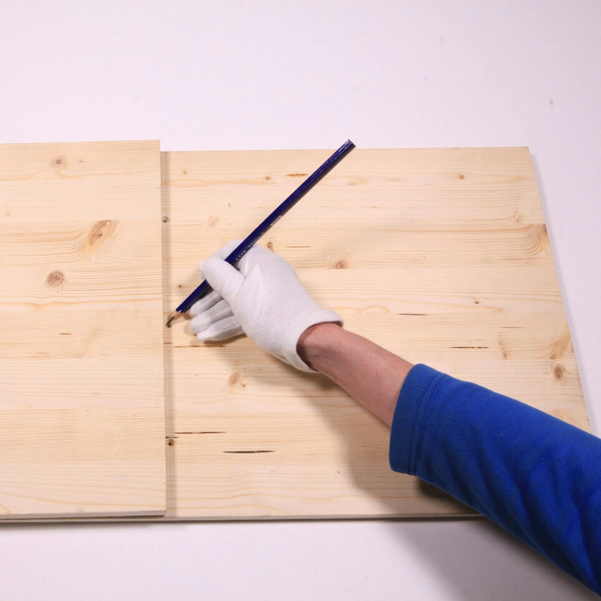 Zweites Holzbrett auf Spielbrett, jemand markiert die Positionen für die Bohrlöcher.