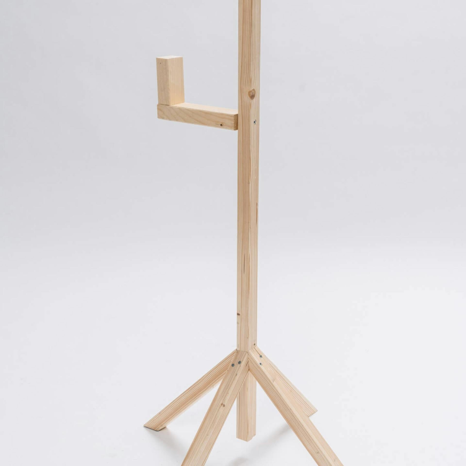 Vor einem hellen Hintergrund steht ein Ständer aus Holz mit vier Holzfüßen. Am oberen Teil des Ständers ist ein Kantholz in L-Form befestigt.