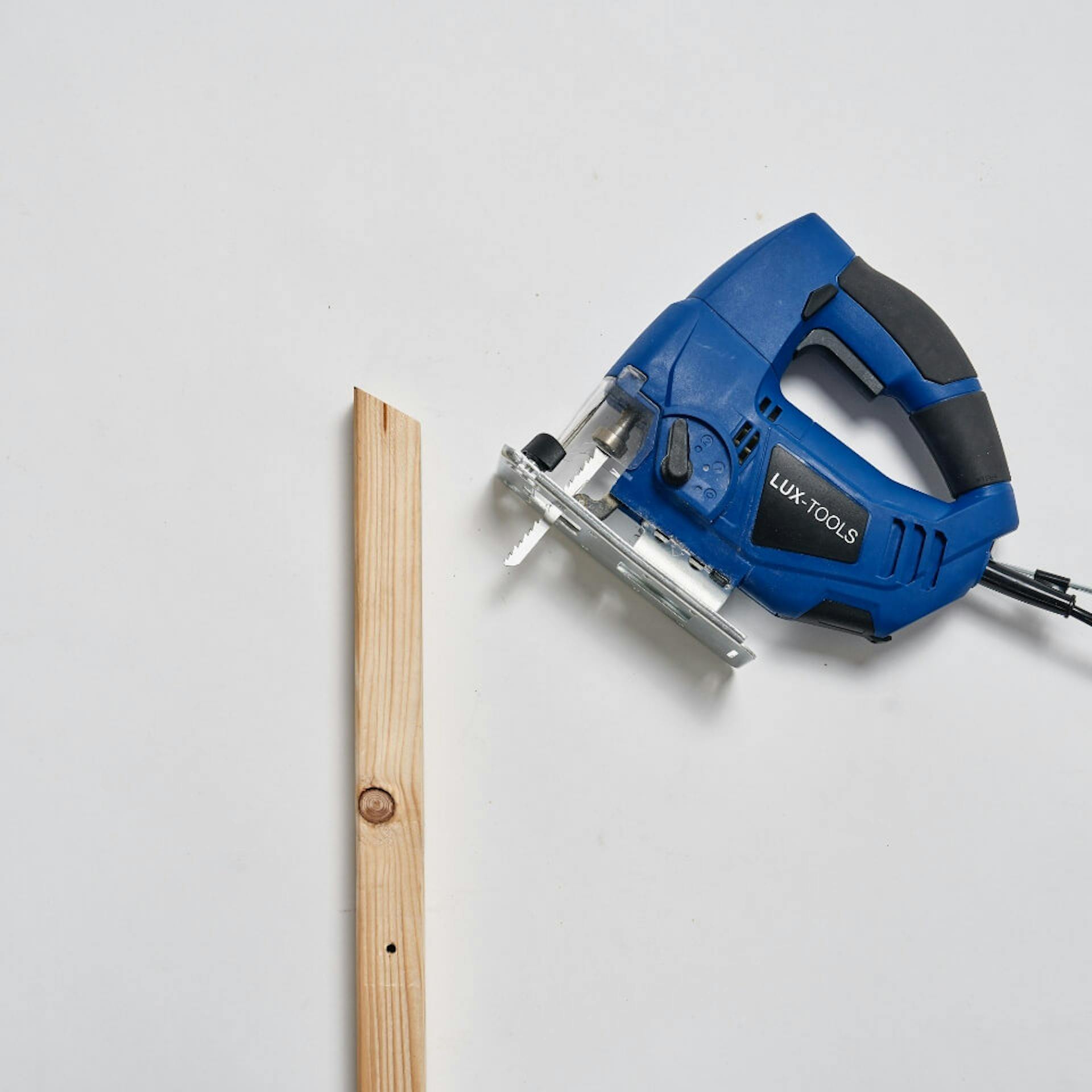 Auf einem hellen Untergrund liegt ein Kantholz. Daneben ist eine blaue Stichsäge zu sehen.