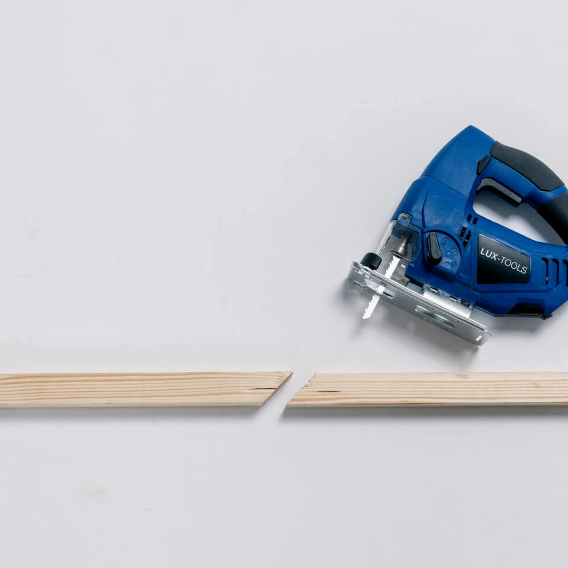 Auf einem hellen Untergrund liegen zwei angeschrägte Kanthölzer. Daneben ist eine blaue Stichsäge zu sehen.