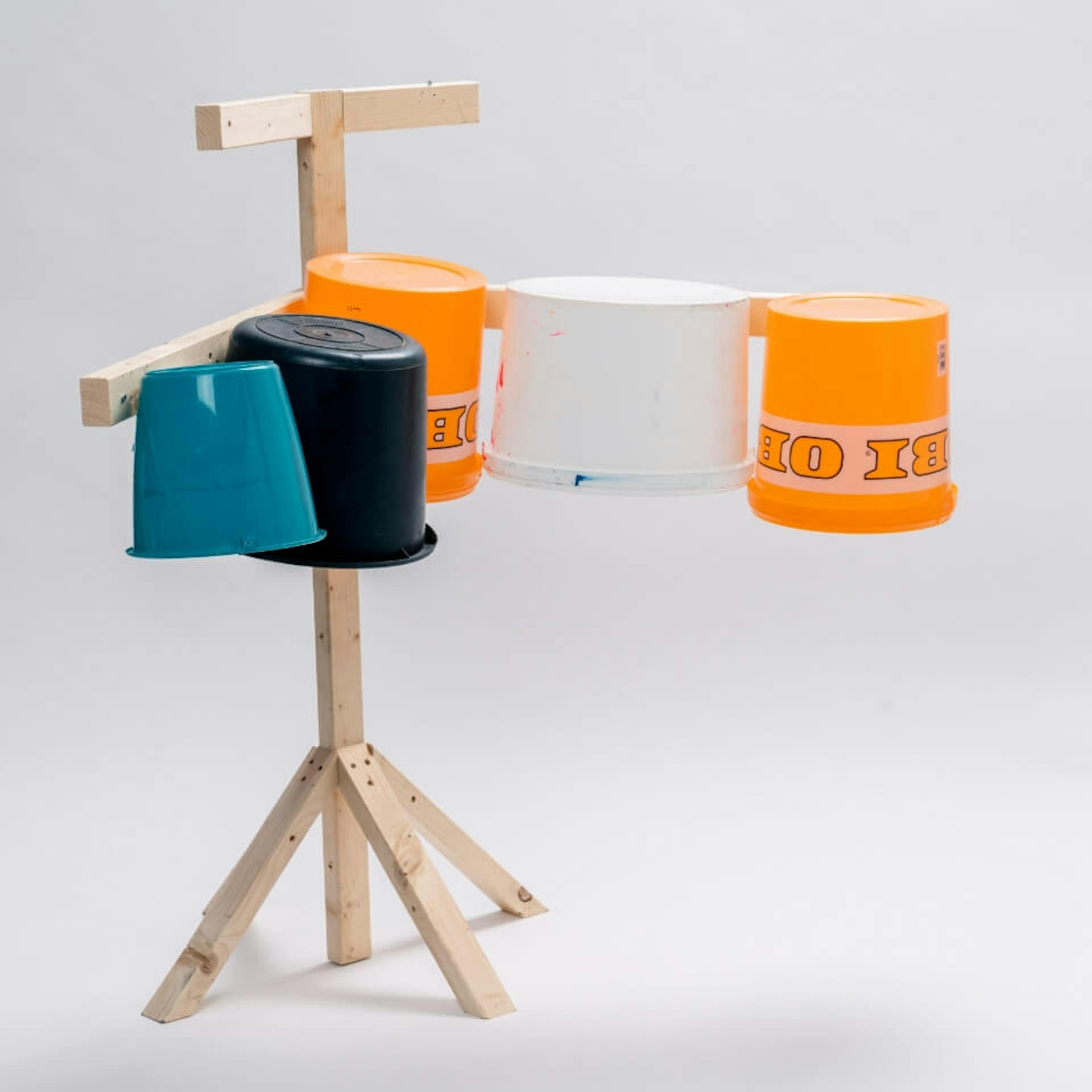 Vor hellem Hintergrund steht ein Ständer aus Holz. An diesem sind mehrere Eimer in verschiedenen Farben befestigt.