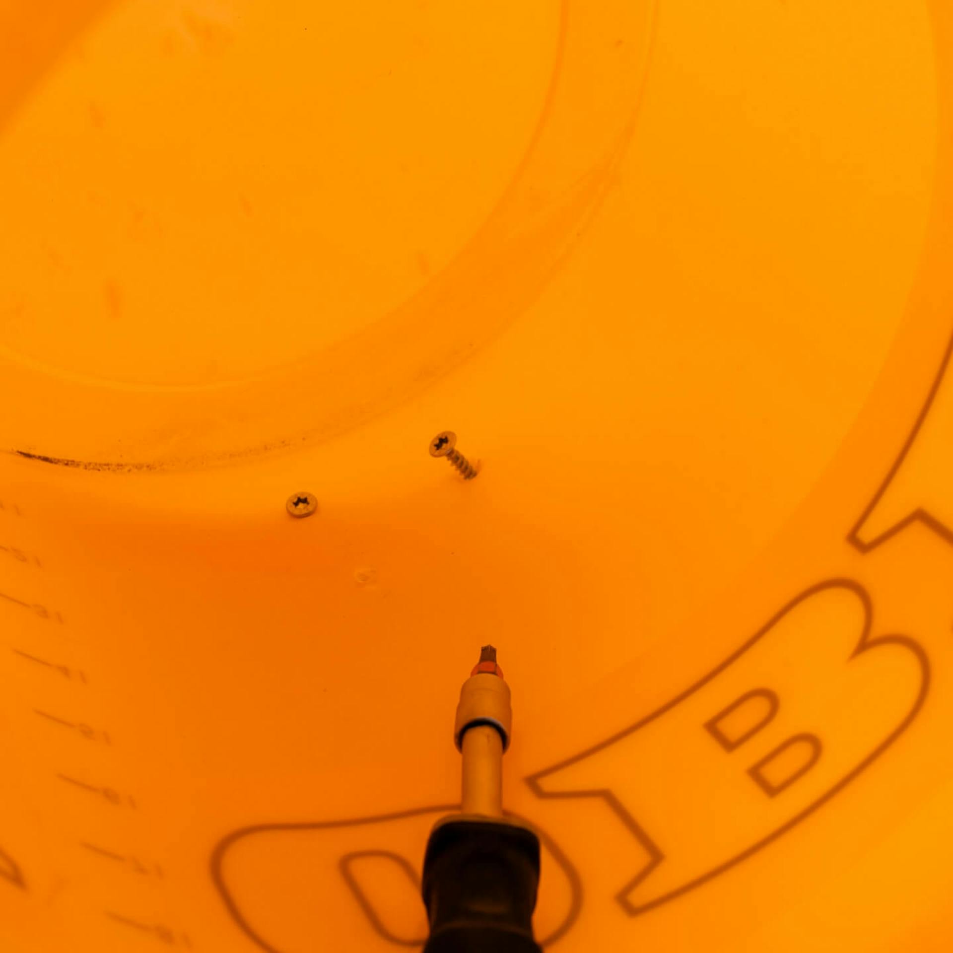 Es ist ein orangener Eimer zu sehen, in welchem zwei Schrauben stecken. Davor ist ein Bohraufsatz zu sehen.