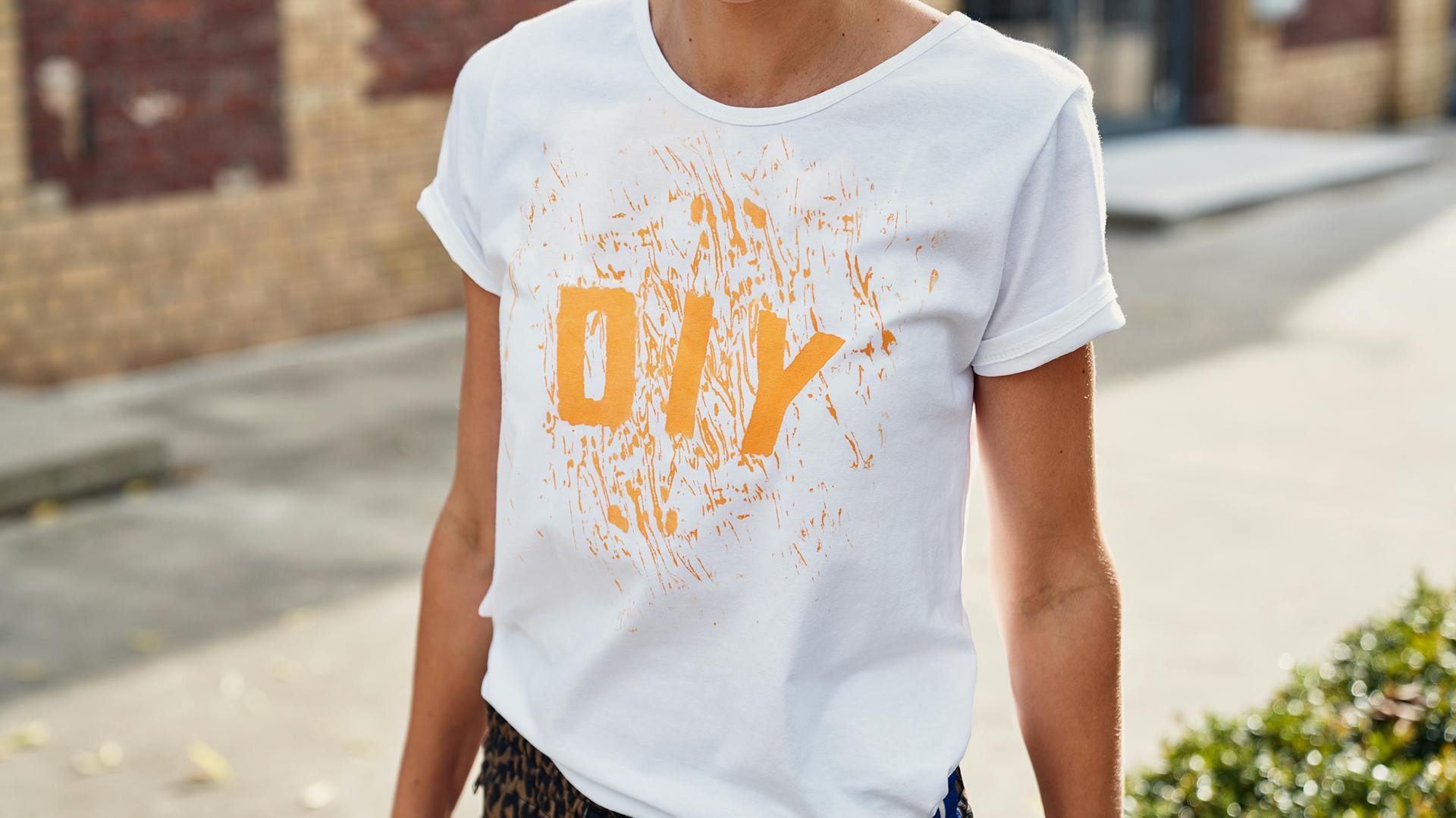 Person mit weißem siebbedrucktem T-Shirt mit gelbem DIY-Schriftzug