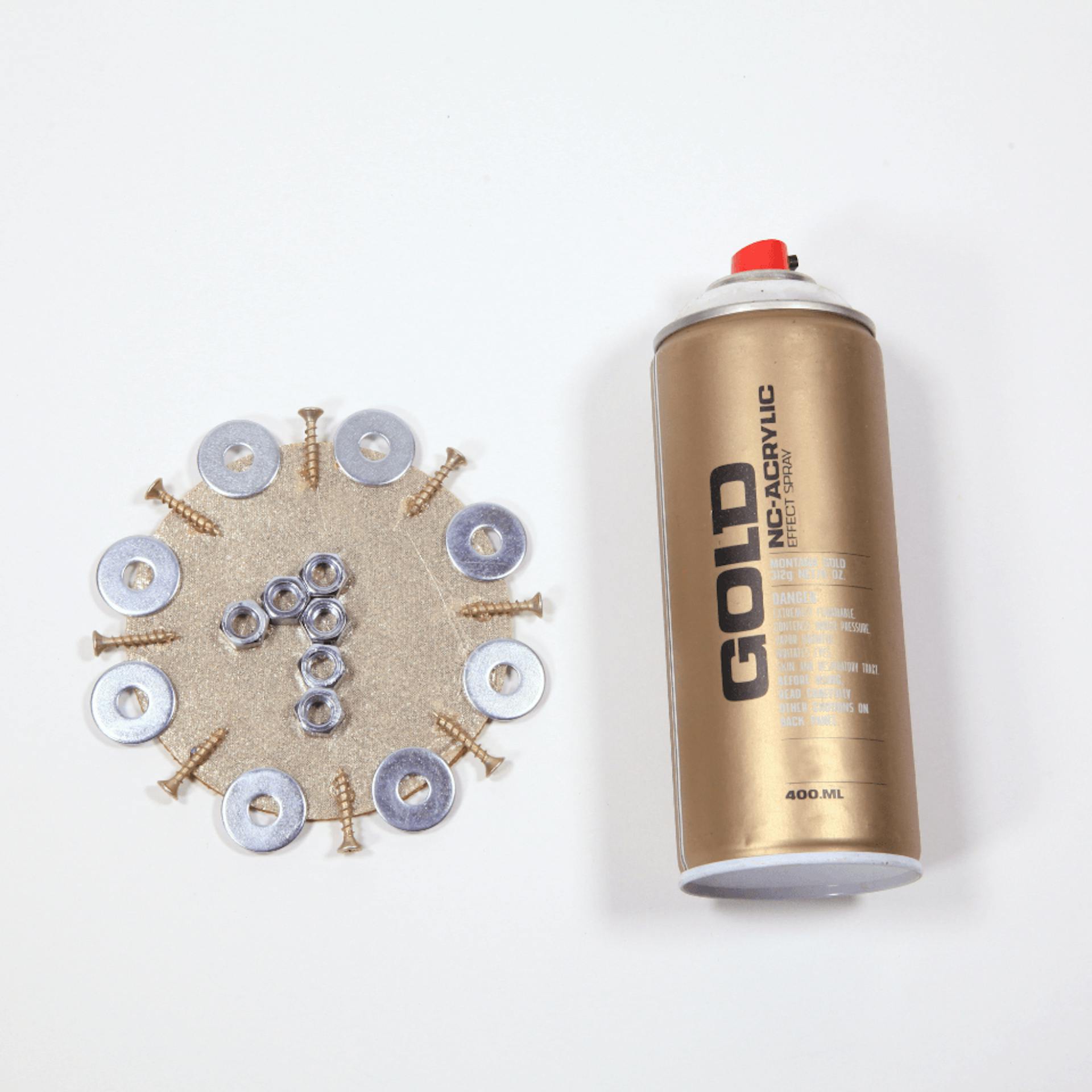 Pappkreis, verziert mit Schrauben, Muttern und Unterlegscheiben, daneben liegt eine Dose mit goldener Sprühfarbe.