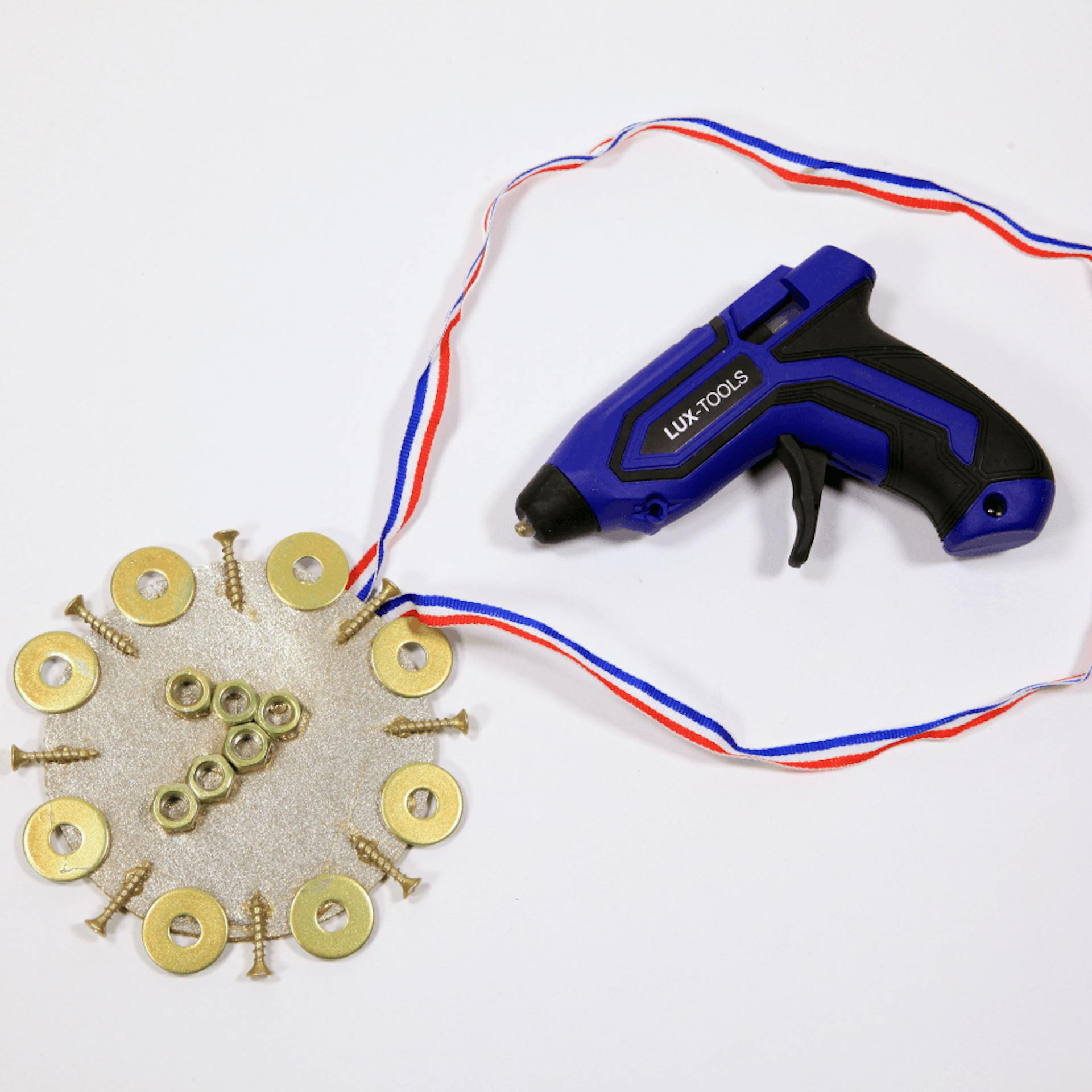 Eine selbst gebastelte Medaille, daneben liegt eine Heißklebepistole.
