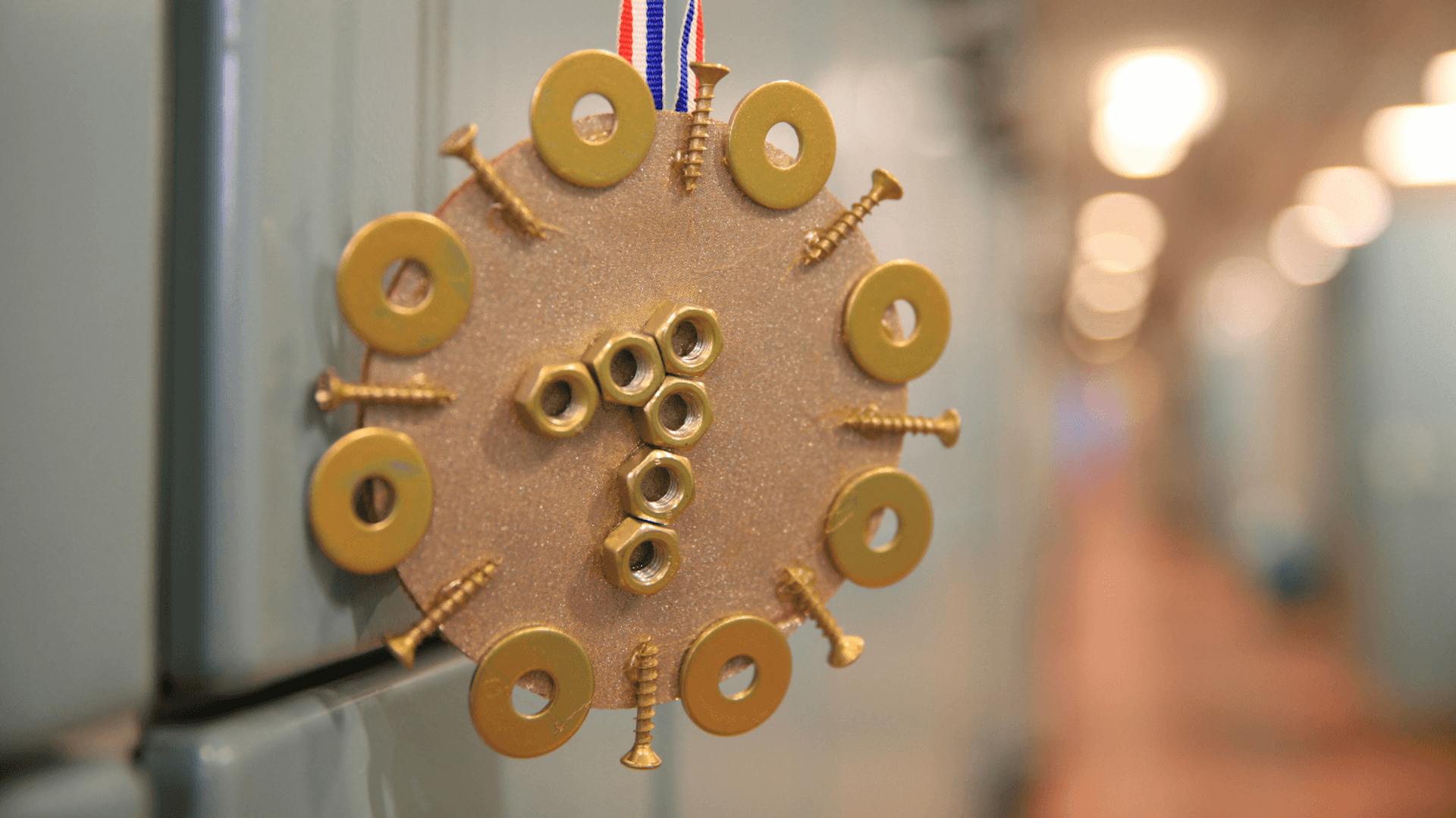 Eine Medaille mit einem blau-weiß-roten Band, verziert mit Schrauben, Muttern und Unterlegscheiben.