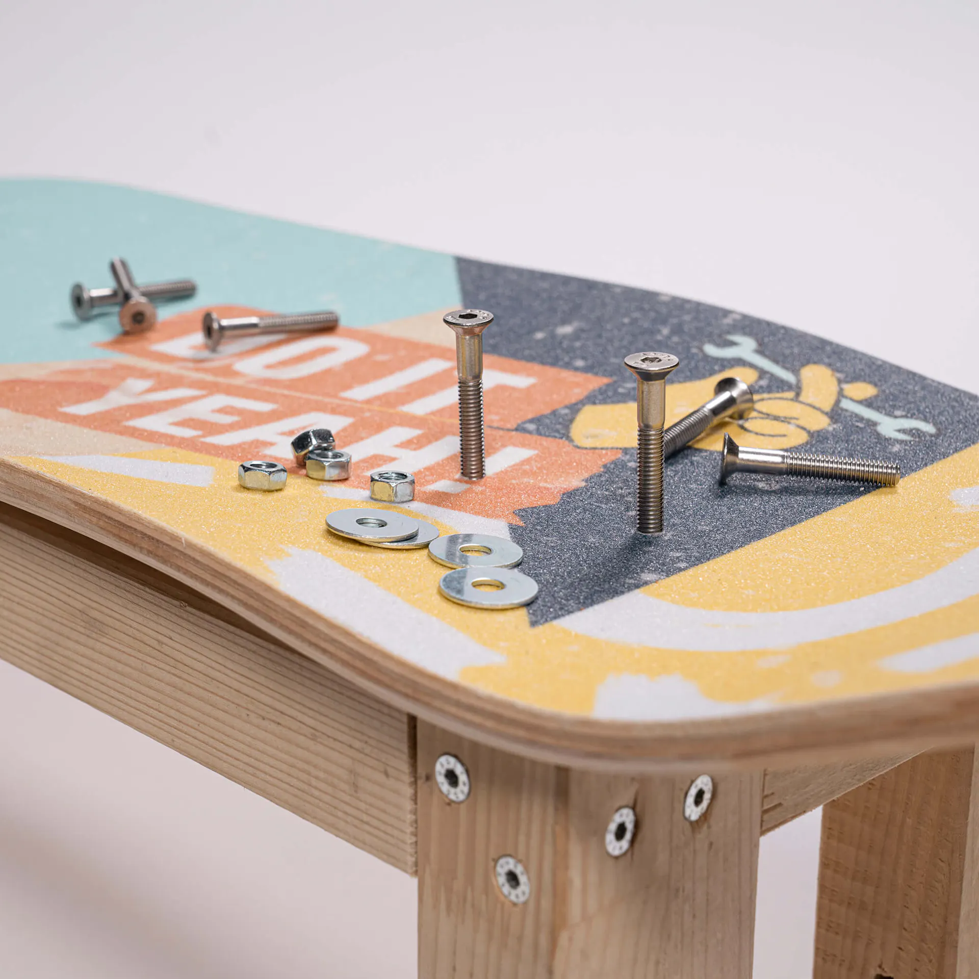 Das Skateboard Deck liegt auf dem Grundgerüst. Es werden Schrauben durch die Löcher gesteckt.
