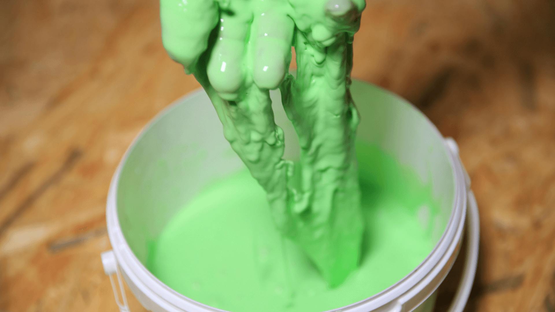 Hand zieht grünen Slime aus Eimer.