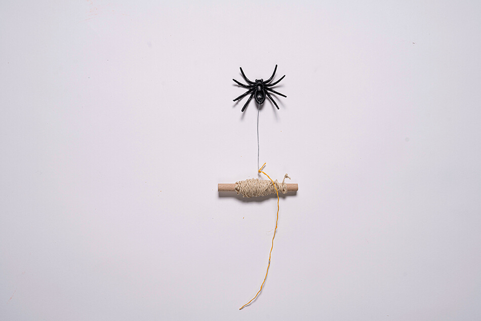 Eine an einem Rundstab befestigte Gummispinne. Am Rundstab und am Draht wurde Schnur befestigt.