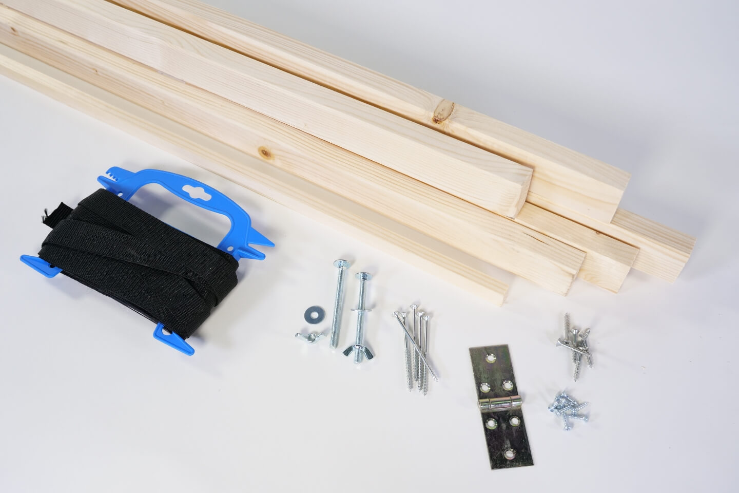  Holzleisten, Gurtband, Schrauben und Scharnier liegen auf einem Tisch.