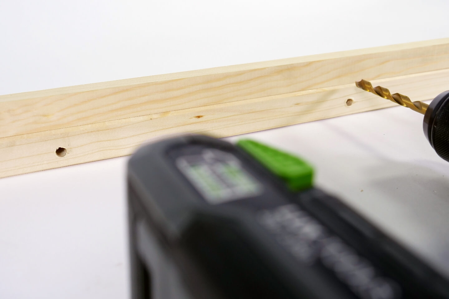 Person bohrt Löcher in Holzleiste.