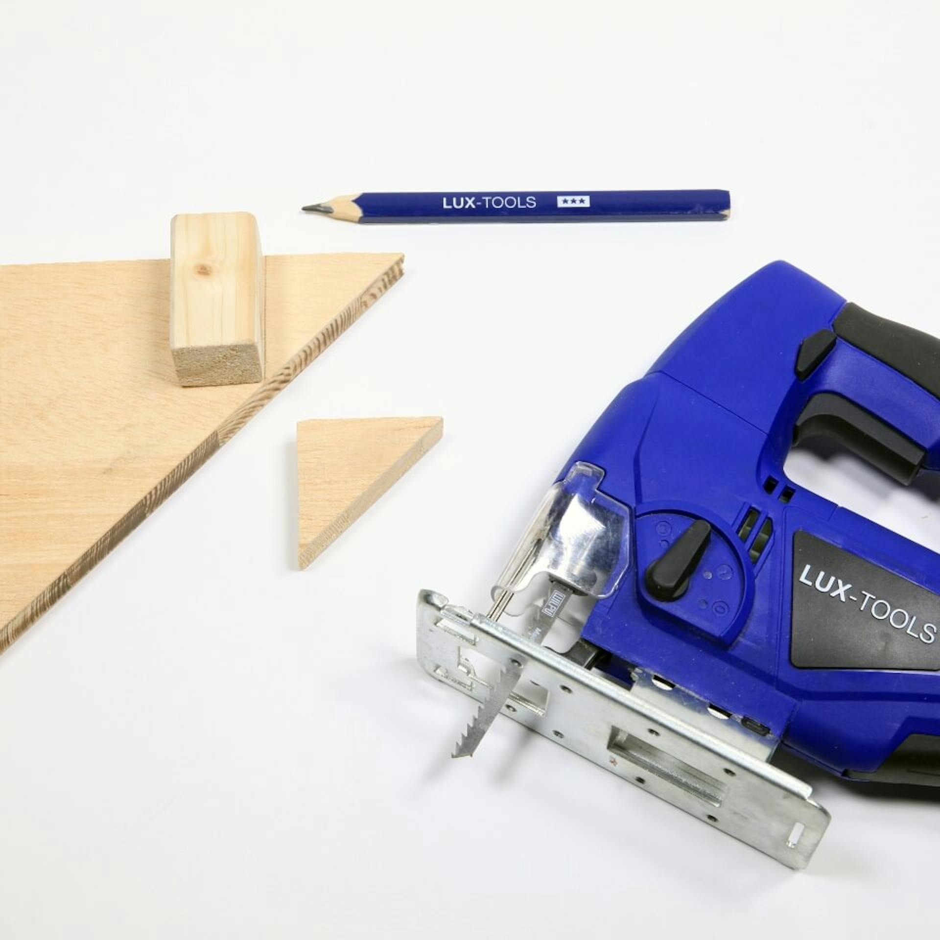 Es ist ein dreieckiges Holzelement zu sehen. Auf diesem liegt ein Holzstück, daneben ist ein kleineres, dreieckiges Holzelement zu sehen. Zudem ist ein blauer Bleistift sowie eine Stichsäge zu sehen.