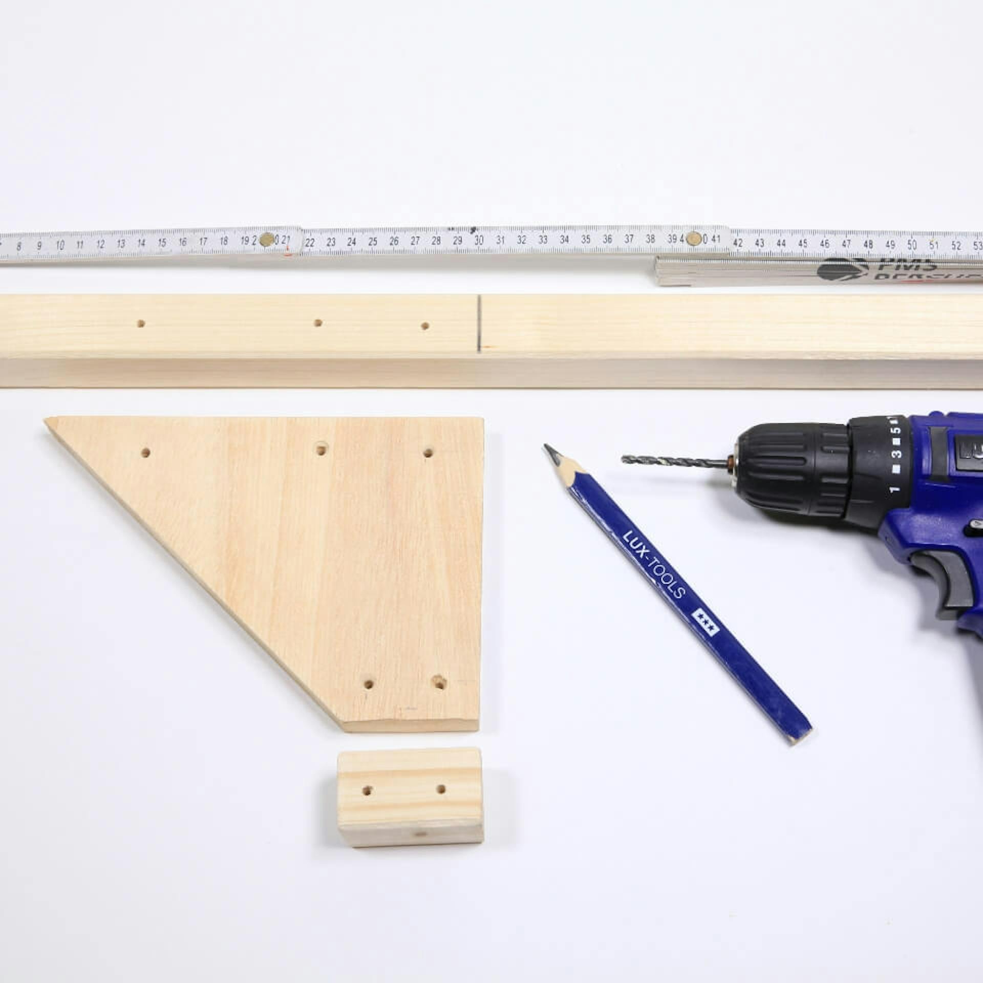 Es sind drei Holzelemente mit Bohrlöchern zu sehen. Daneben liegen ein Zollstock, ein Bleistift und ein Akkuschrauber.