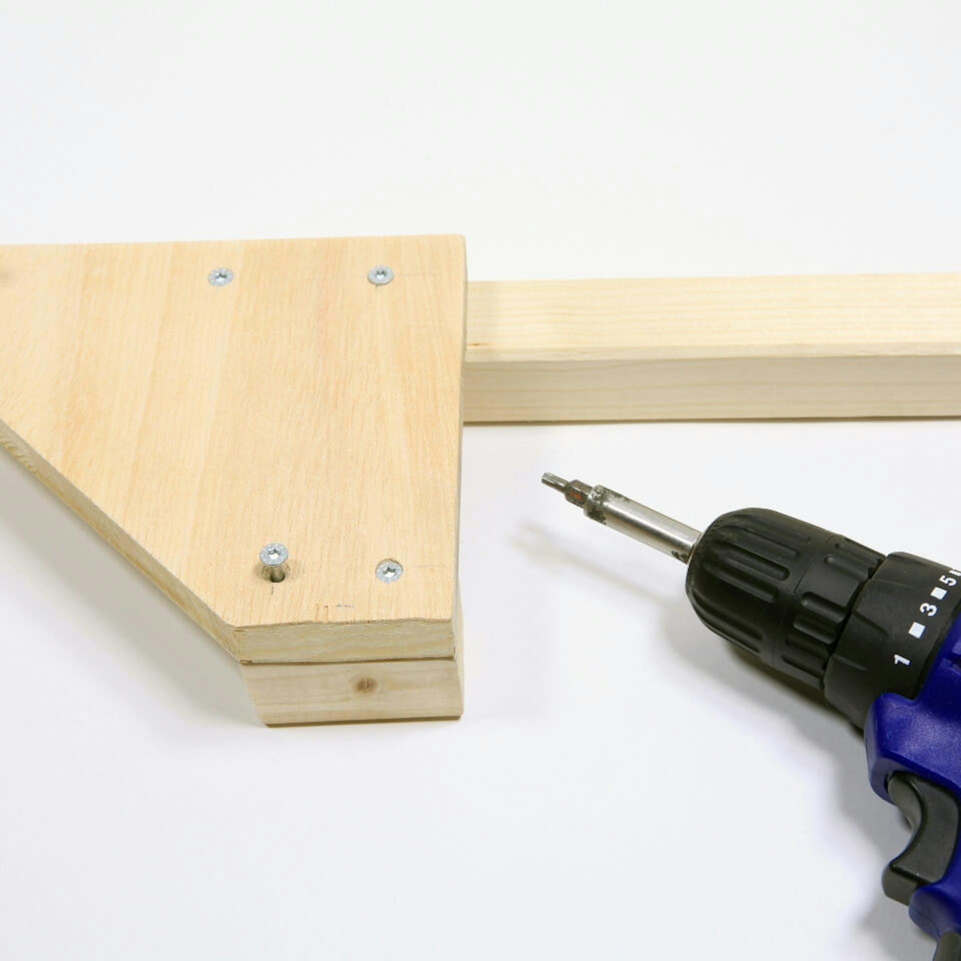 Es ist ein Holzelement zu sehen, welches mit Schrauben an einem Kantholz befestigt ist. Daneben ist ein blauer Akkuschrauber zu sehen.