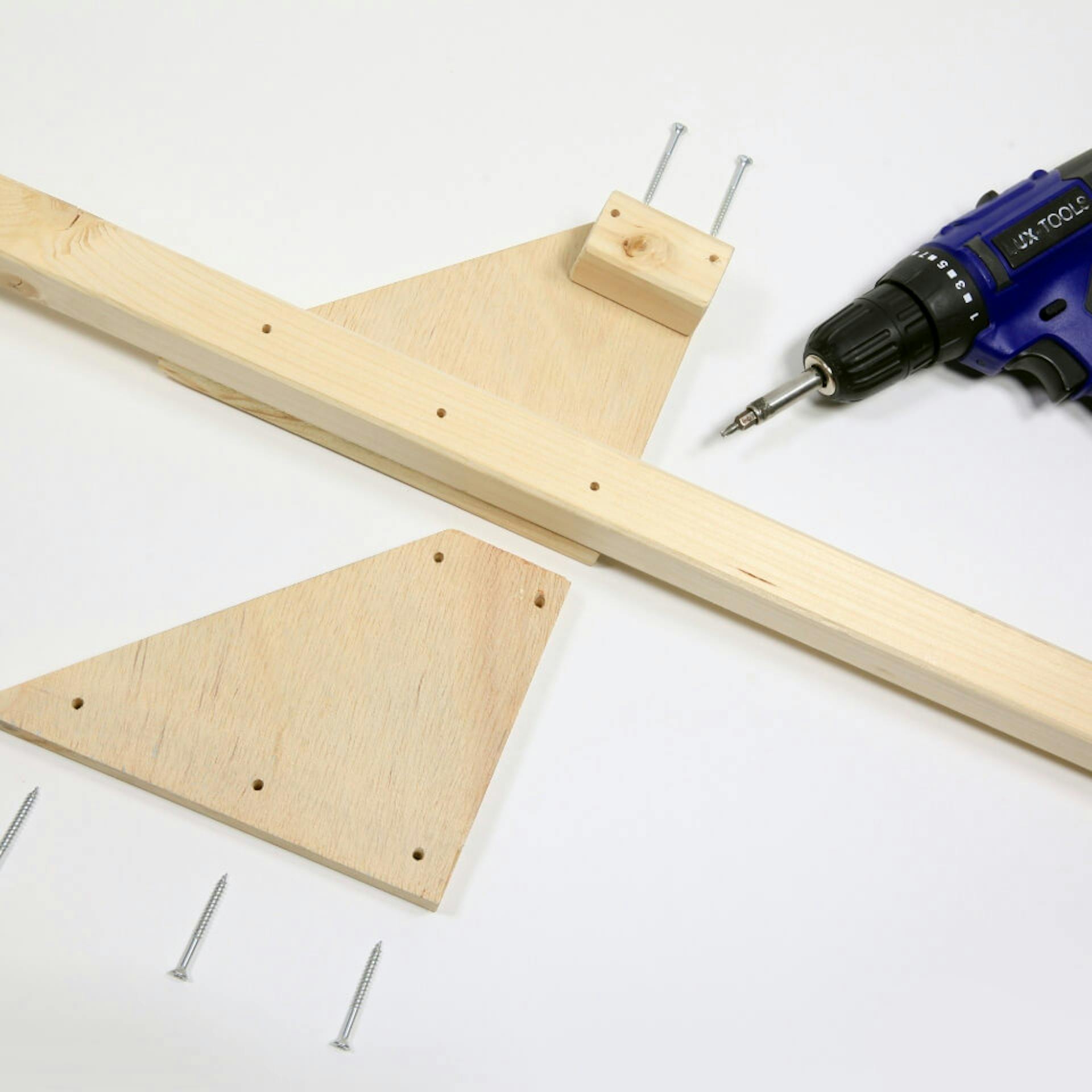 Es sind mehrere Holzelemente mit Bohrlöchern sowie fünf Schrauben zu sehen. Daneben liegt ein blauer Akkuschrauber.