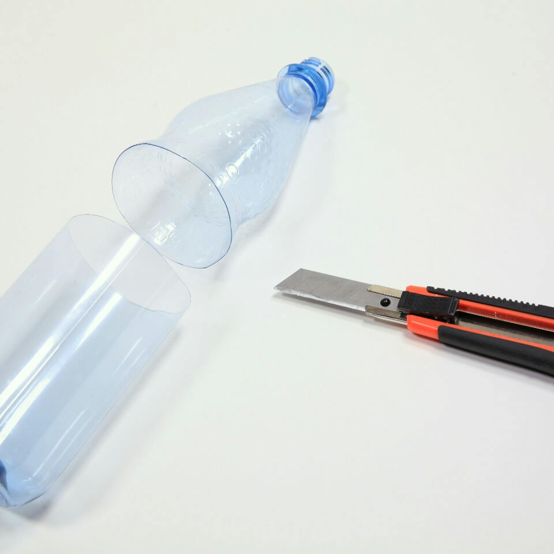 Es ist eine Plastikflasche zu sehen, welche mittig durchtrennt wurde. Daneben liegt ein Cutter.