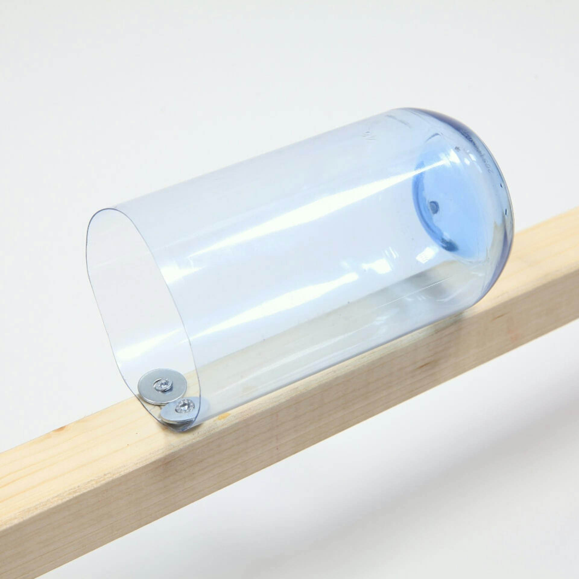 Es ist ein Kantholz zu sehen, an welchem mit zwei Schrauben die untere Hälfte einer Plastikflasche befestigt wurde.