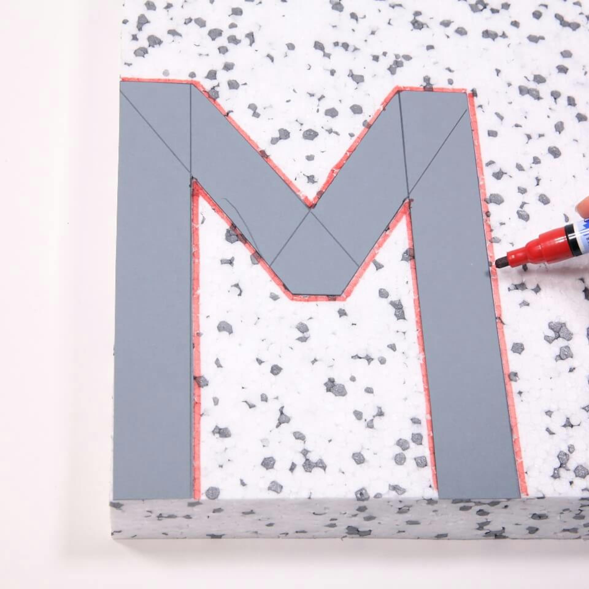 Die ausgeschnittene Schablone liegt auf dem Styropor. Eine Person überträgt die Form.