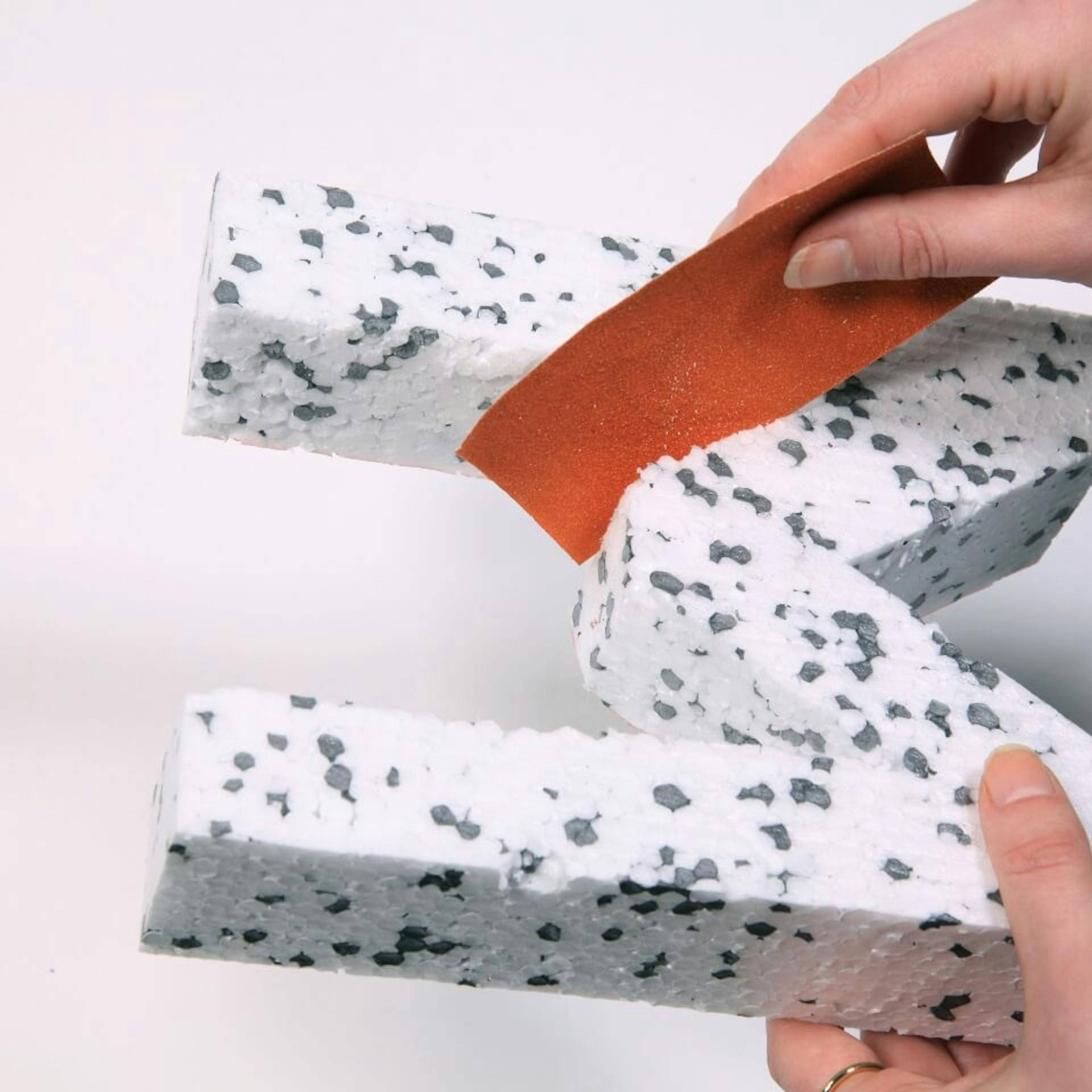 Eine Person schleift die Styropor-Figur mit einem Stück Schleifpapier ab.