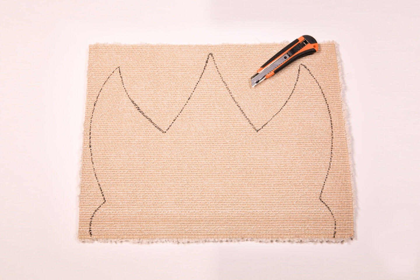 Tappeto quadrato con corona disegnata accanto a un taglierino.