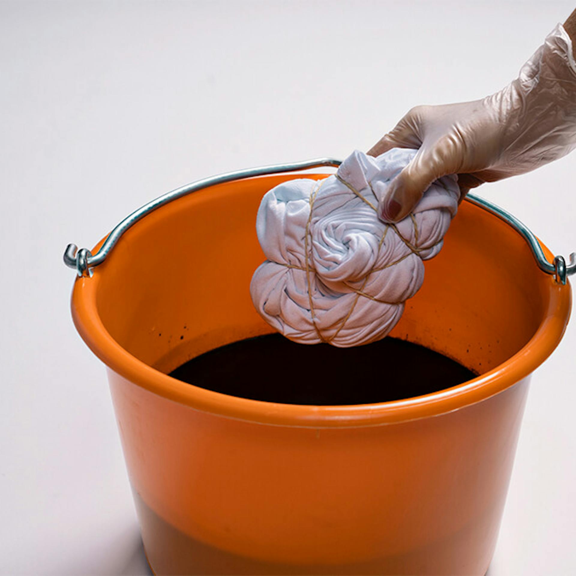 Eine Person tunkt ein abgebundenes Shirt in einen Eimer mit Textilfarbe.