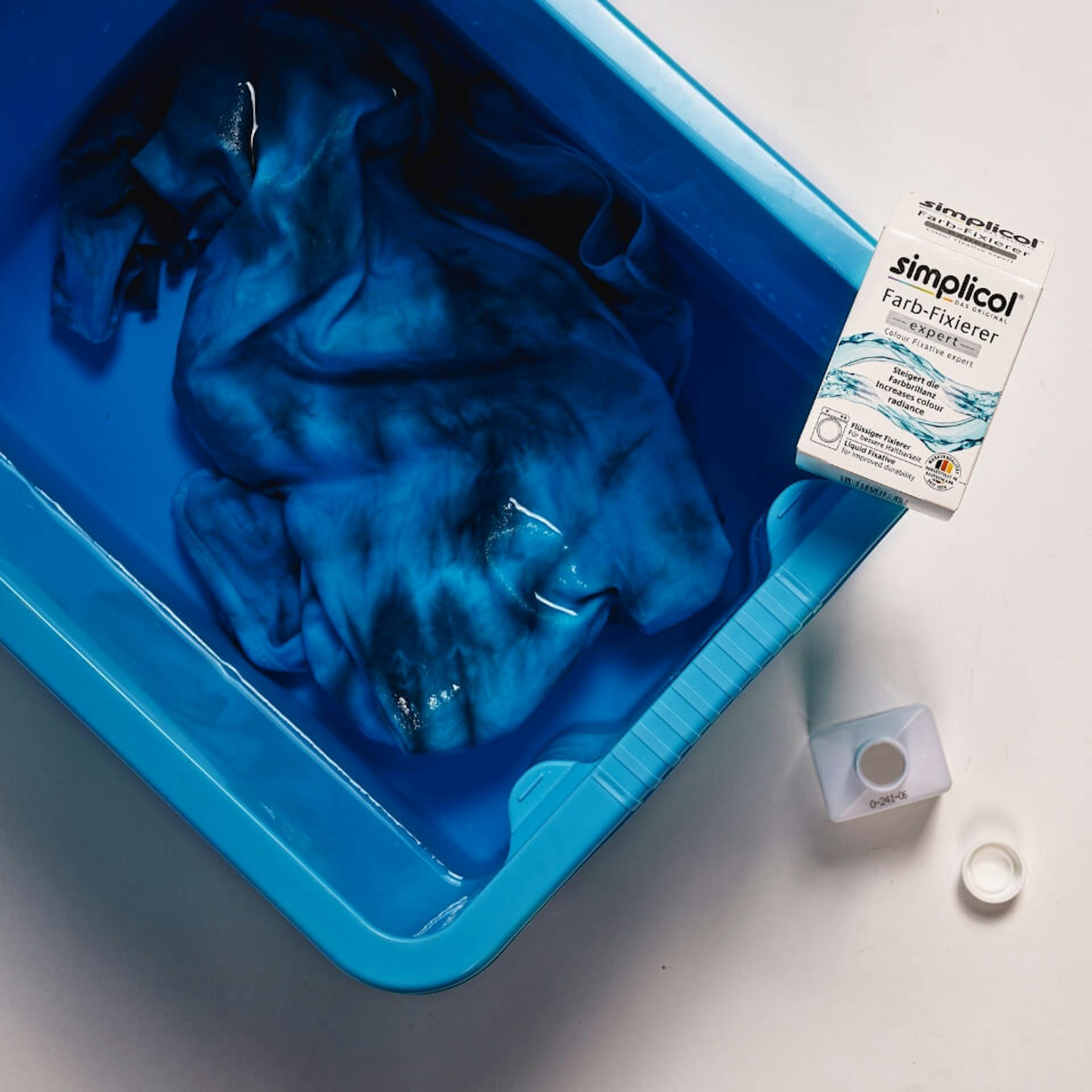 Gefärbtes T-Shirt liegt in einer mit Wasser und Fixiersalz gefüllten Wanne.