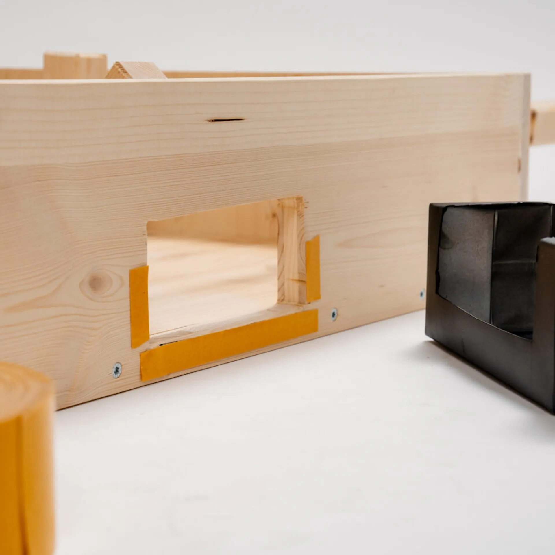 Oboustranná páska na brankovém otvoru stolního fotbálku, na přední straně je role oboustranné pásky, na druhé straně je rozříznutý černý nápojový karton.