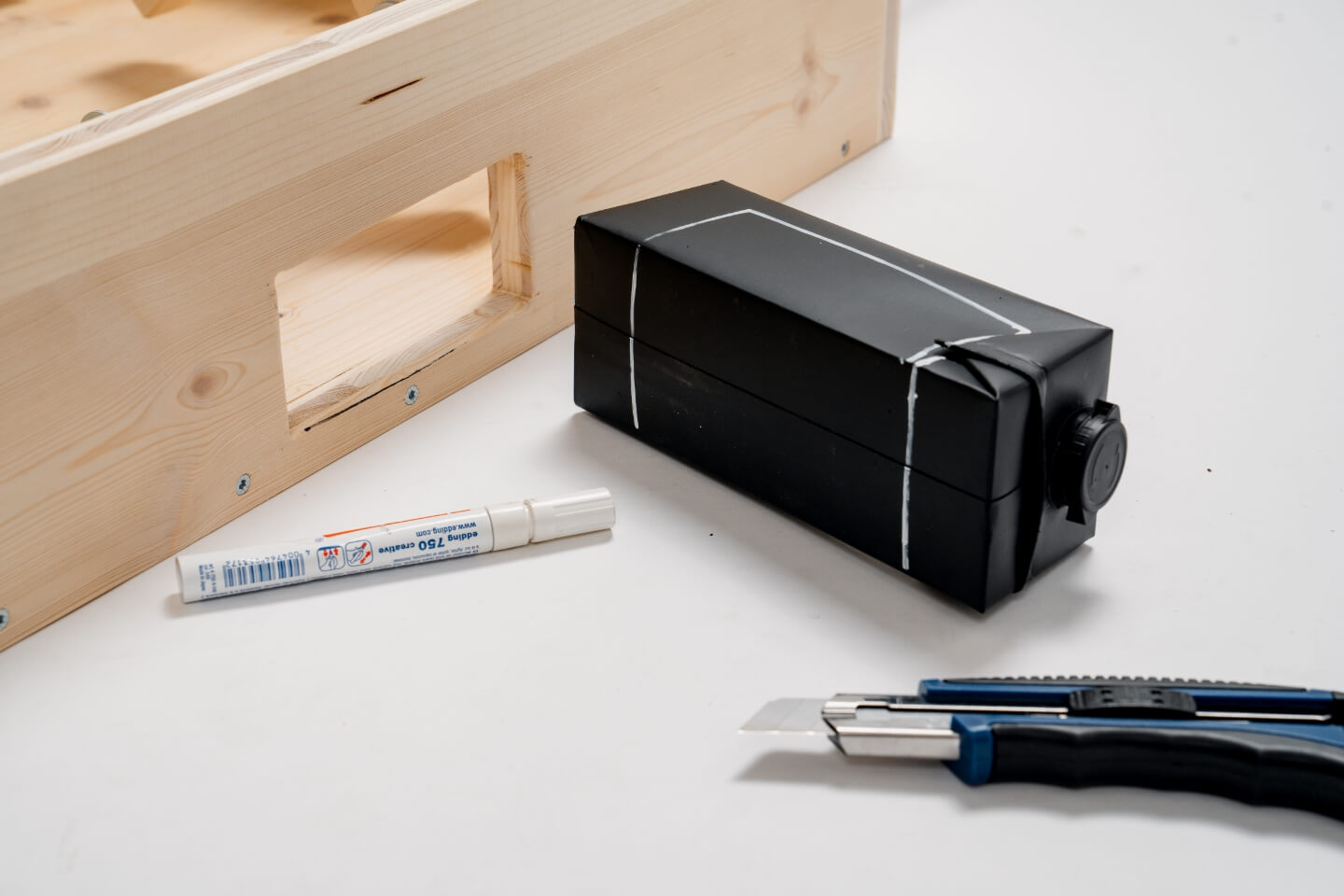 Černý karton s bílými čarami nakreslenými na stolní fotbal, vedle něj je permanentní fix a řezačka.