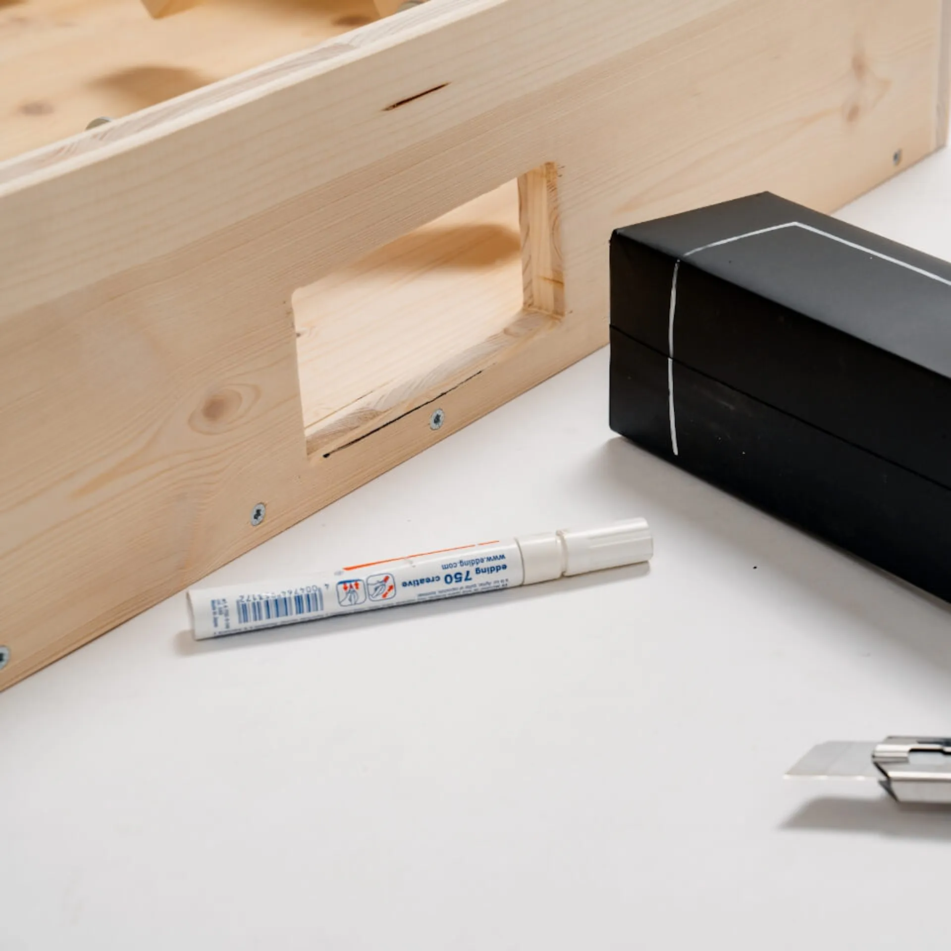 Černý karton s bílými čarami nakreslenými na stolní fotbal, vedle něj je permanentní fix a řezačka.