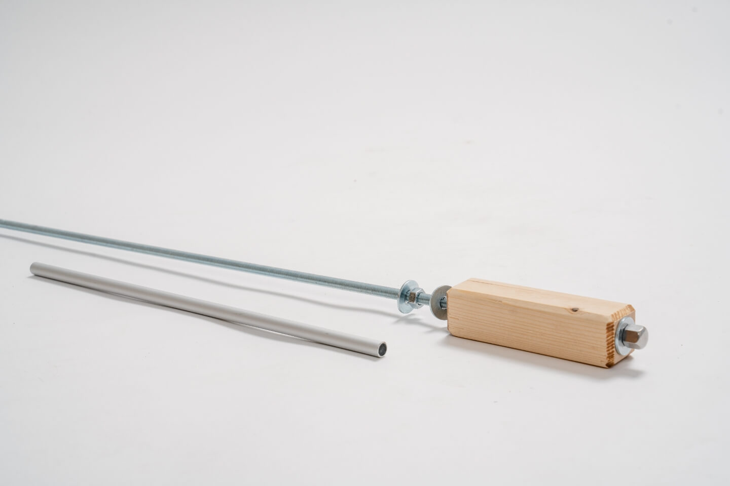 Závitová tyč s hranolem, maticemi a podložkami. Před ním je hliníková trubka.