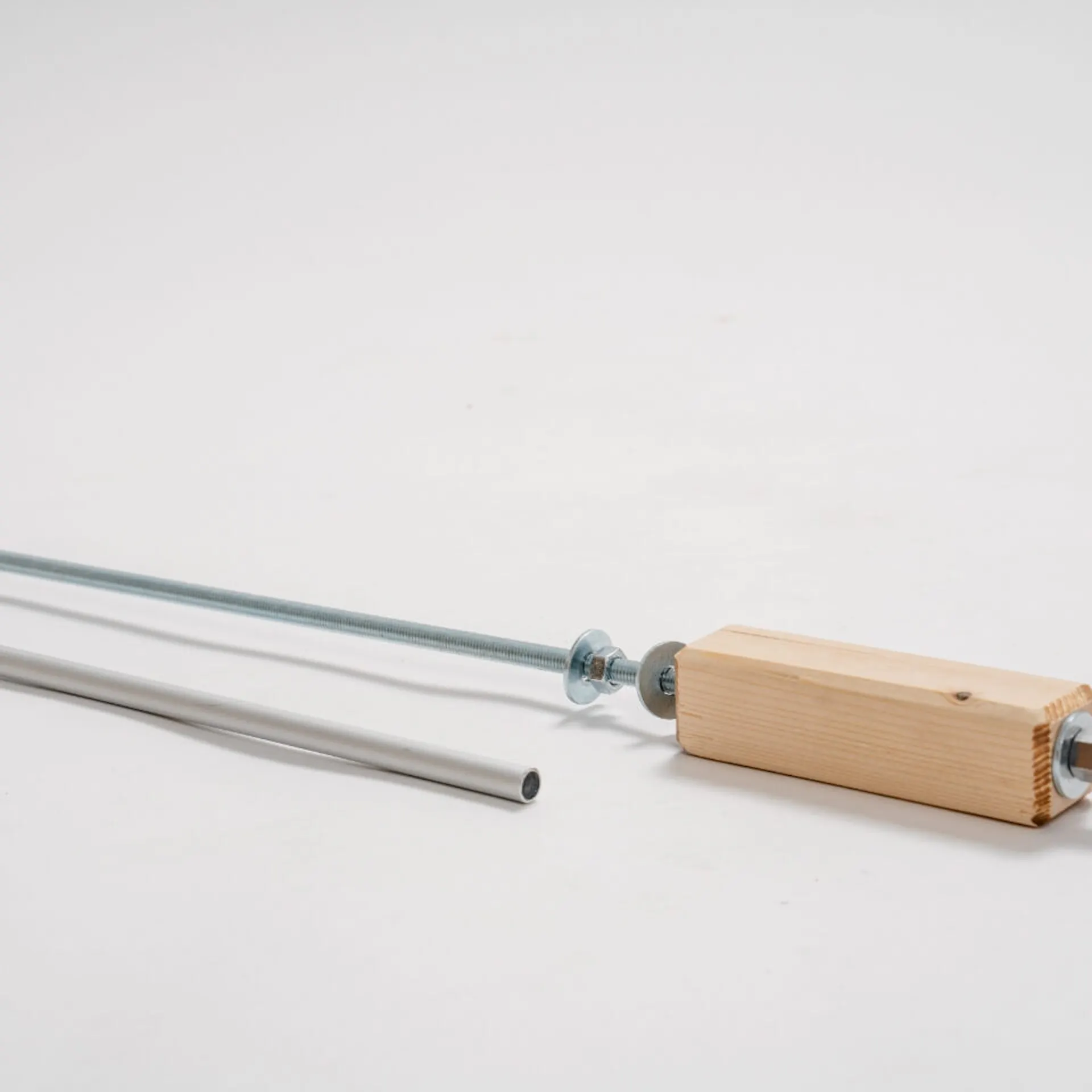 Závitová tyč s hranolem, maticemi a podložkami. Před ním je hliníková trubka.