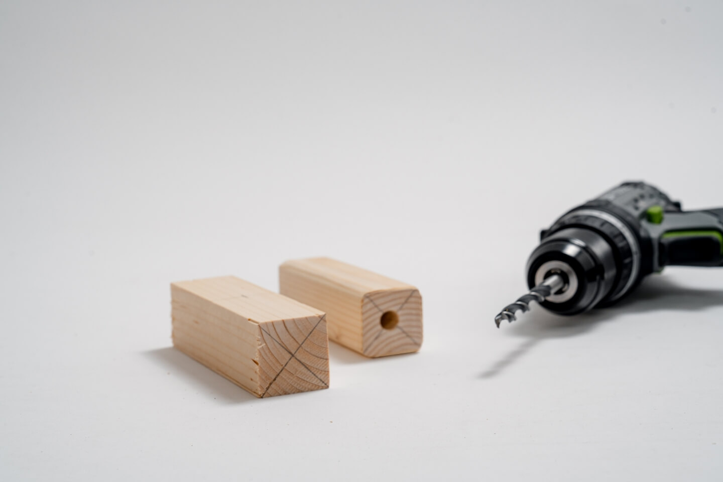 Dva hranoly, na jednom hranolu byl nakreslen kříž, na druhém hranolu byla vyvrtána díra. Vedle je akumulátorový šroubovák.