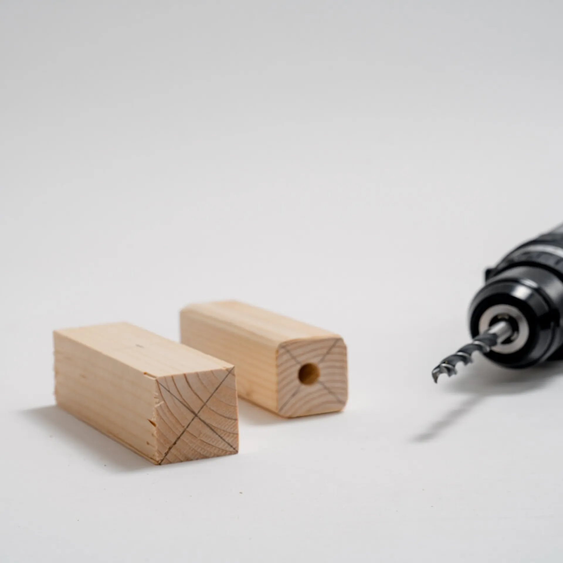 Dva hranoly, na jednom hranolu byl nakreslen kříž, na druhém hranolu byla vyvrtána díra. Vedle je akumulátorový šroubovák.