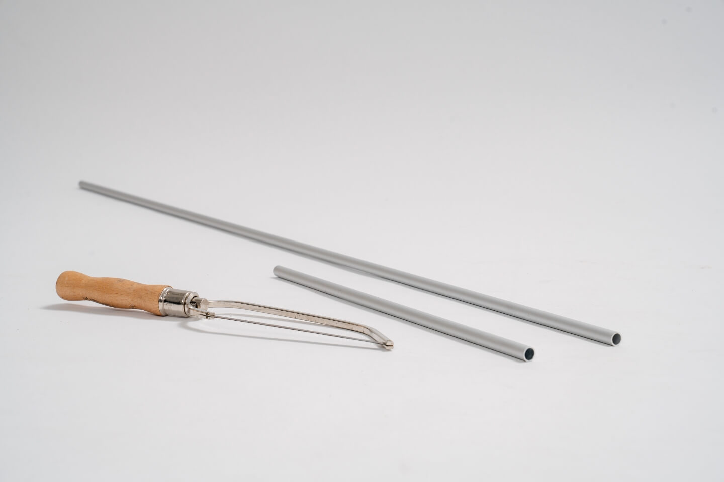 Dvě hliníkové trubky různých délek, před nimi je pila na železo.