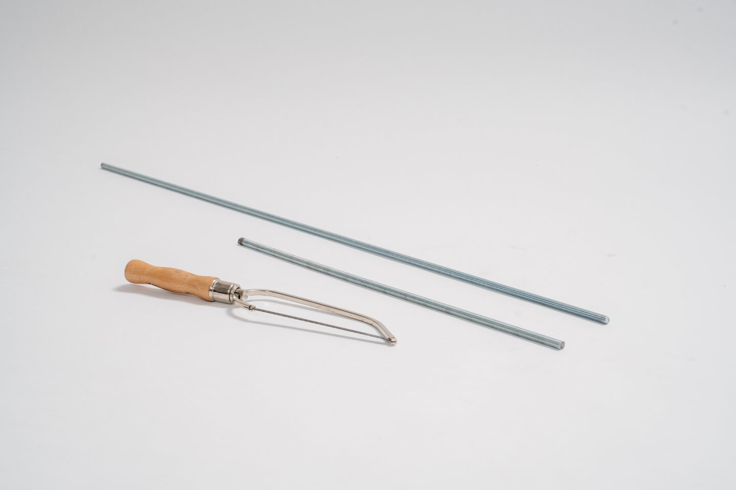 Dvě různě dlouhé závitové tyče, před nimi je pila na železo.