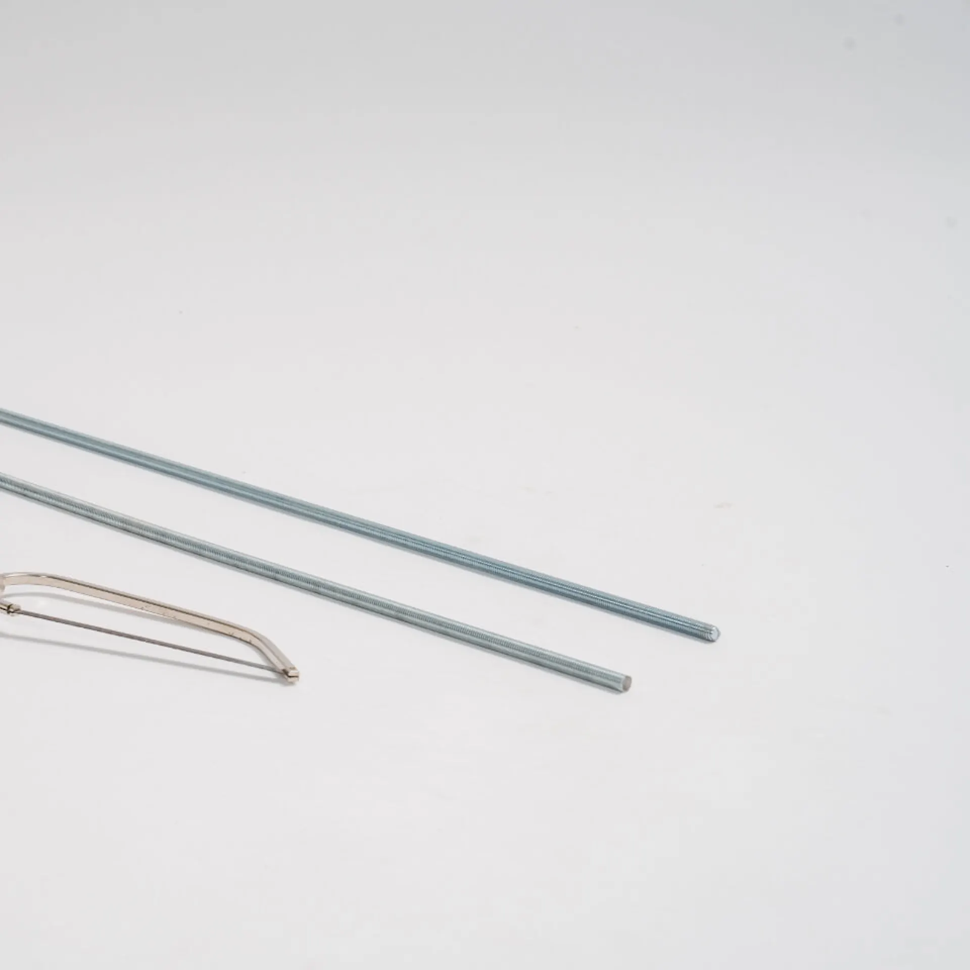 Dvě různě dlouhé závitové tyče, před nimi je pila na železo.