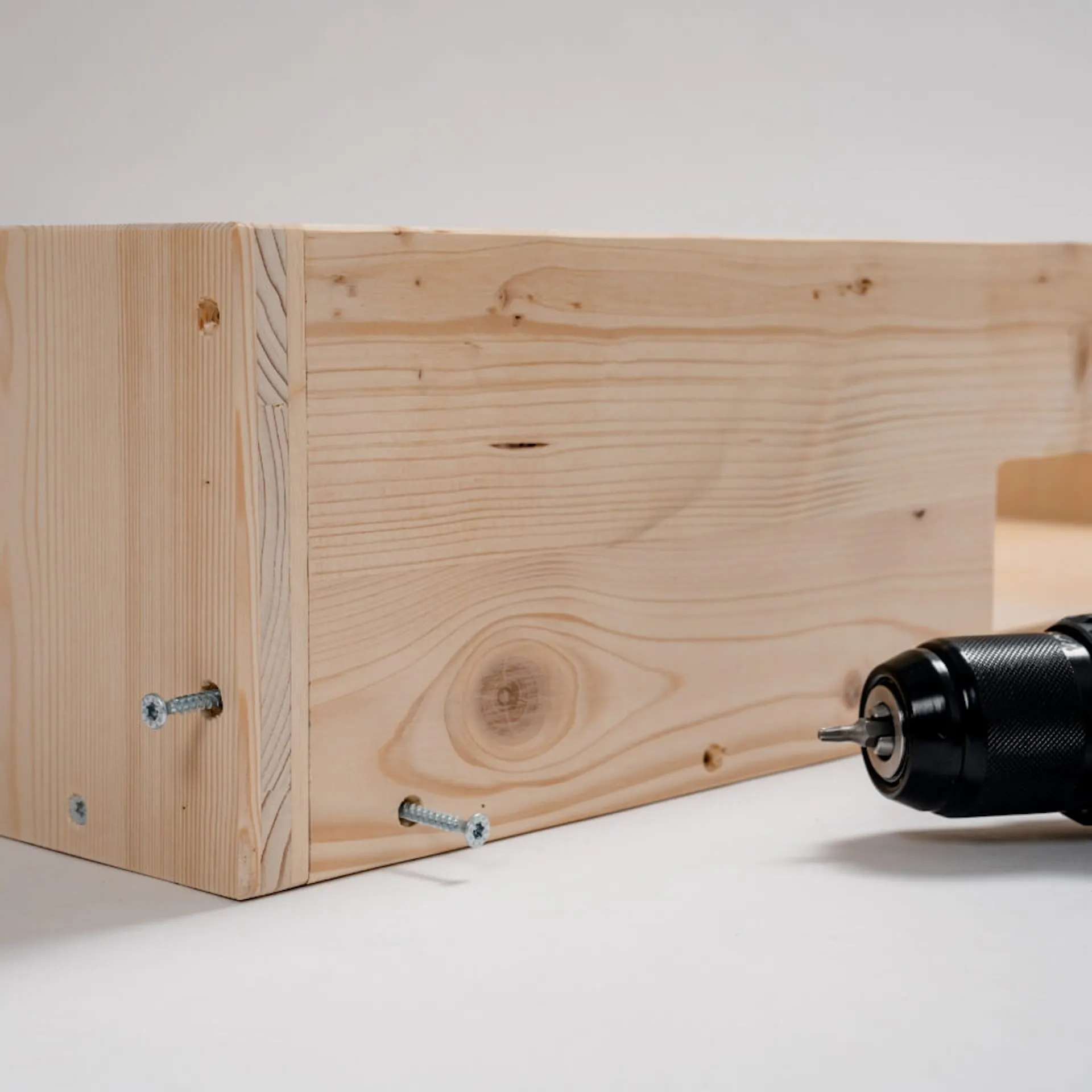 Přišroubované dřevěné desky, některé šrouby nejsou zašroubovány. Vedle je akumulátorový šroubovák.