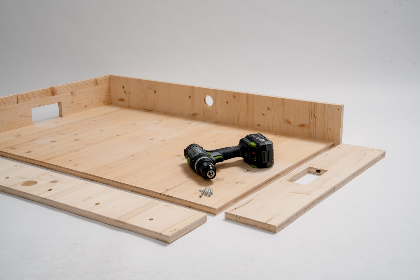 Velká deska, na ní jsou připevněny dvě desky, dvě desky leží vedle. Na desce je aku šroubovák a nějaké šroubky.