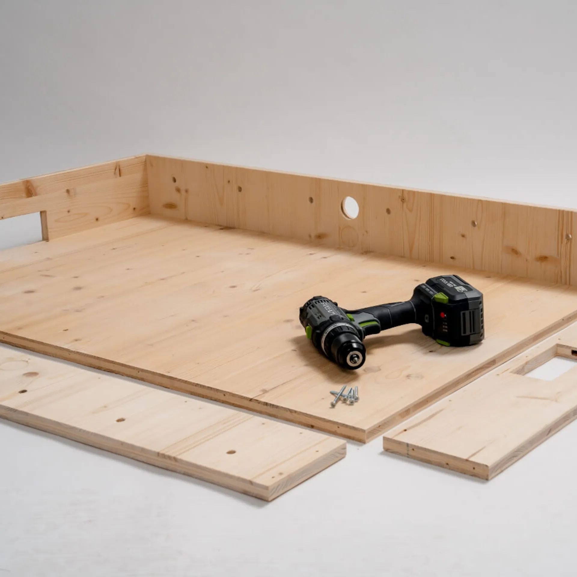 Velká deska, na ní jsou připevněny dvě desky, dvě desky leží vedle. Na desce je aku šroubovák a nějaké šroubky.