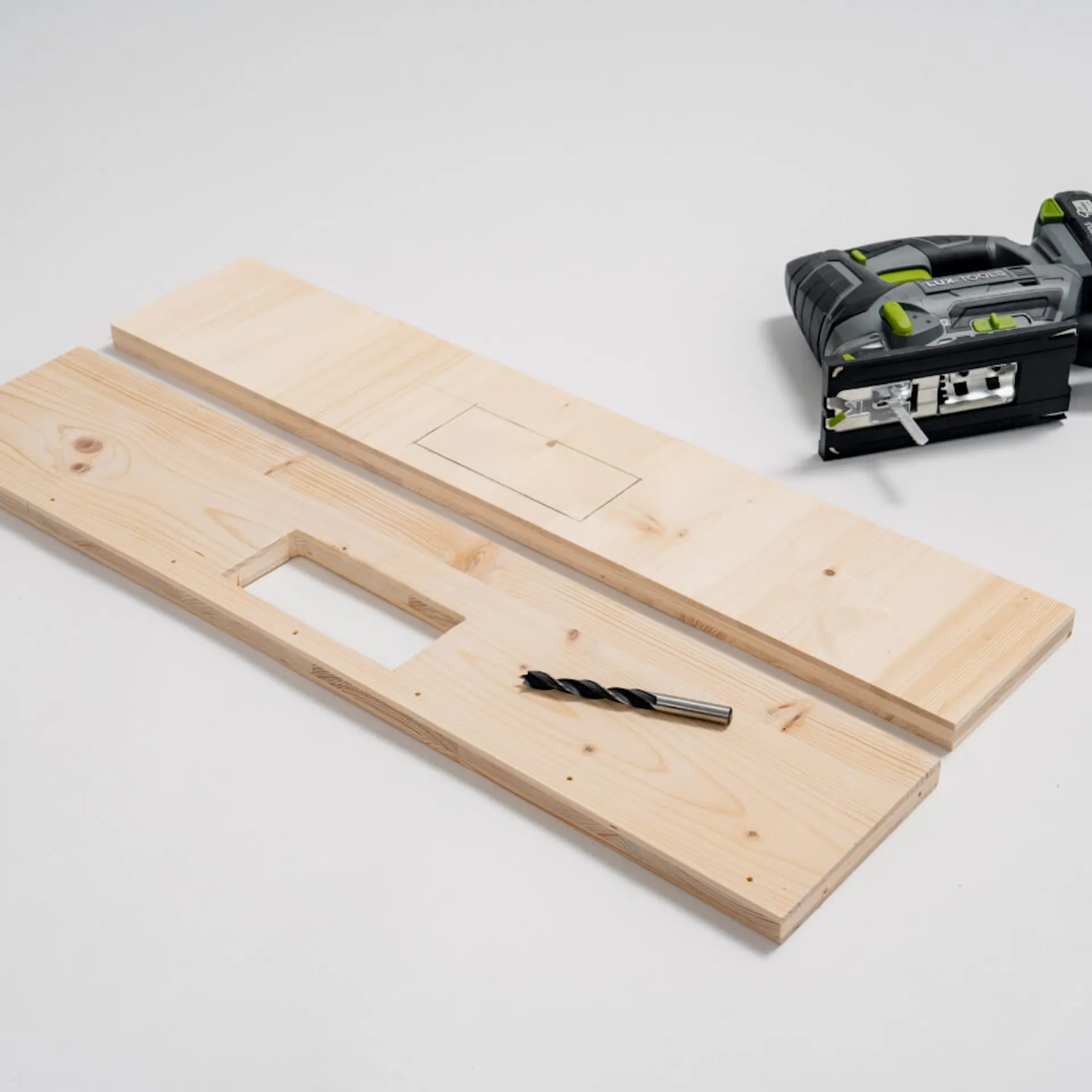 Dvě desky, v jedné z desek je vyříznutý obdélník. Na desce leží vrták. Za deskami leží skládačka.