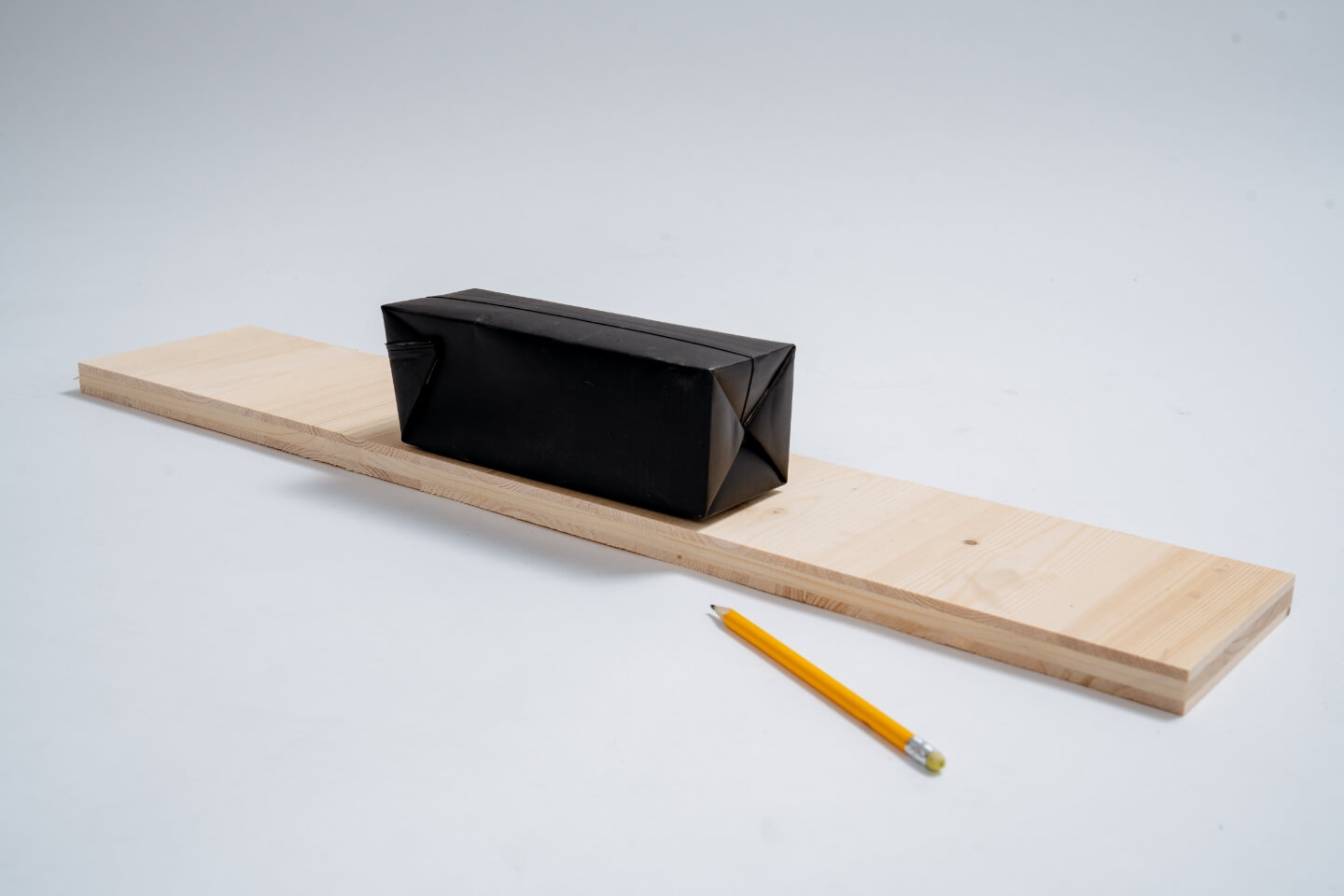 Dřevěná deska s černým tetra packem. Před ním je tužka.