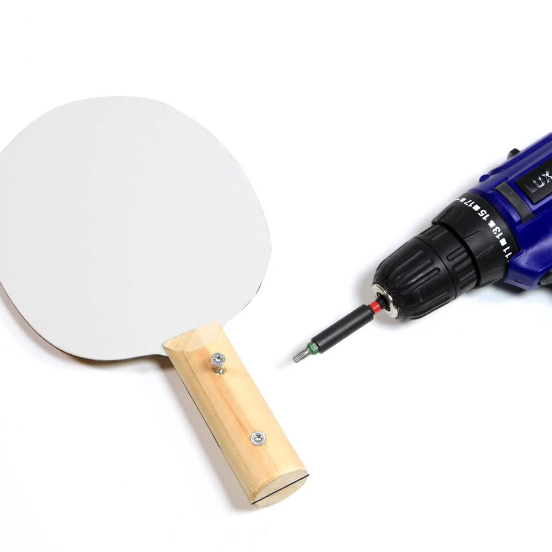 Der verschraubte Tischtennisschläger und der Akkuschrauber liegen auf einem weißen Untergrund.