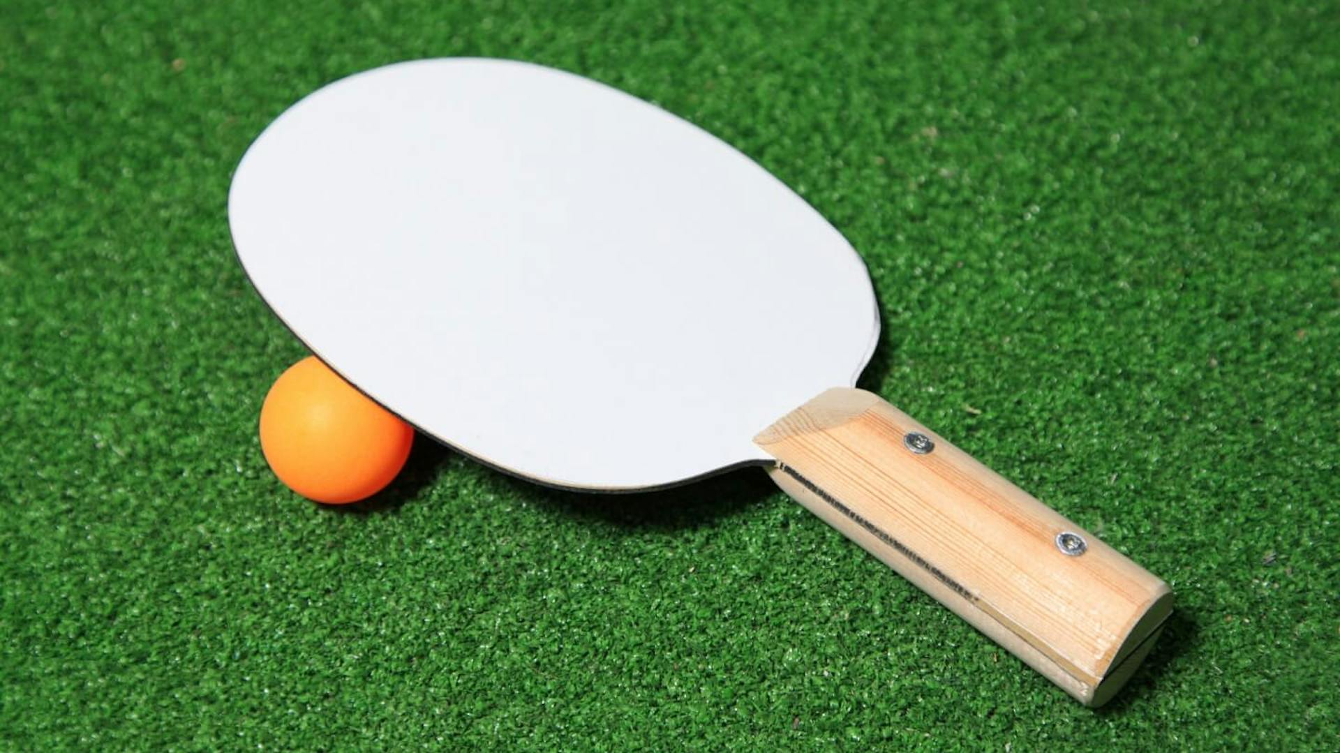 Der fertige Tischtennisschläger liegt mit einem Ball auf Kunstrasen.